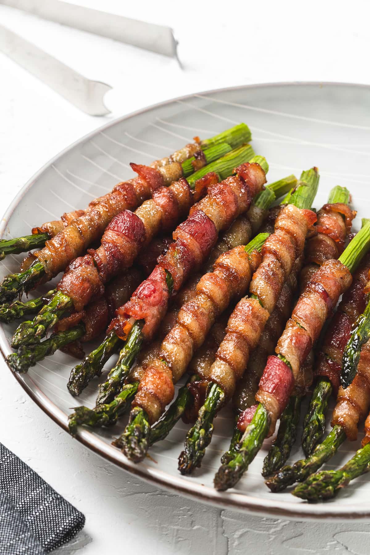 Bacon-wrapped asparagus on a grey plate with vertical white lines.