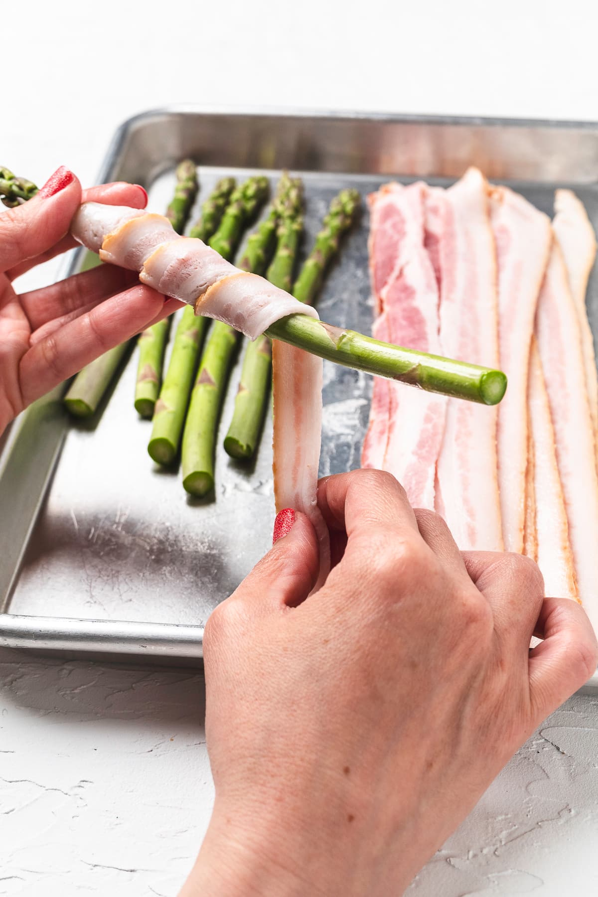 Hands wrapping bacon around asparagus.