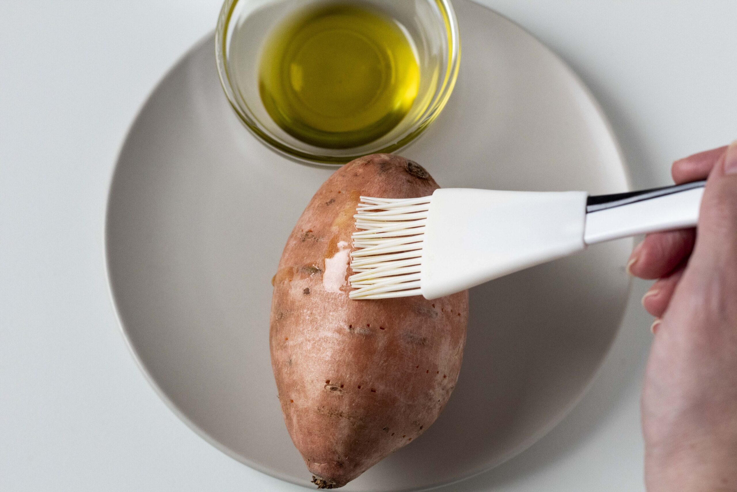 Hand brushing sweet potato with olive oil.