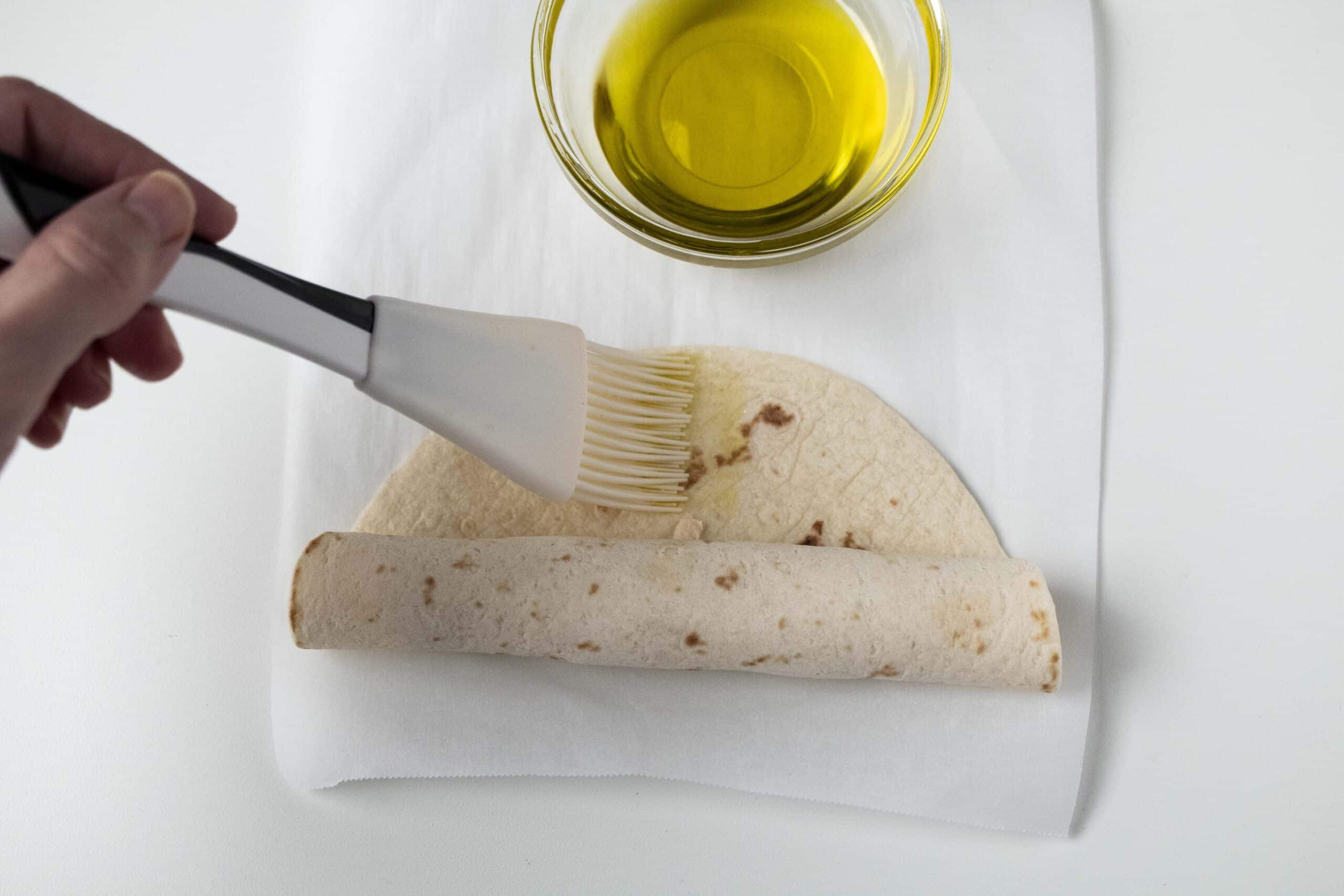 Olive oil being brushed on to a taquito.