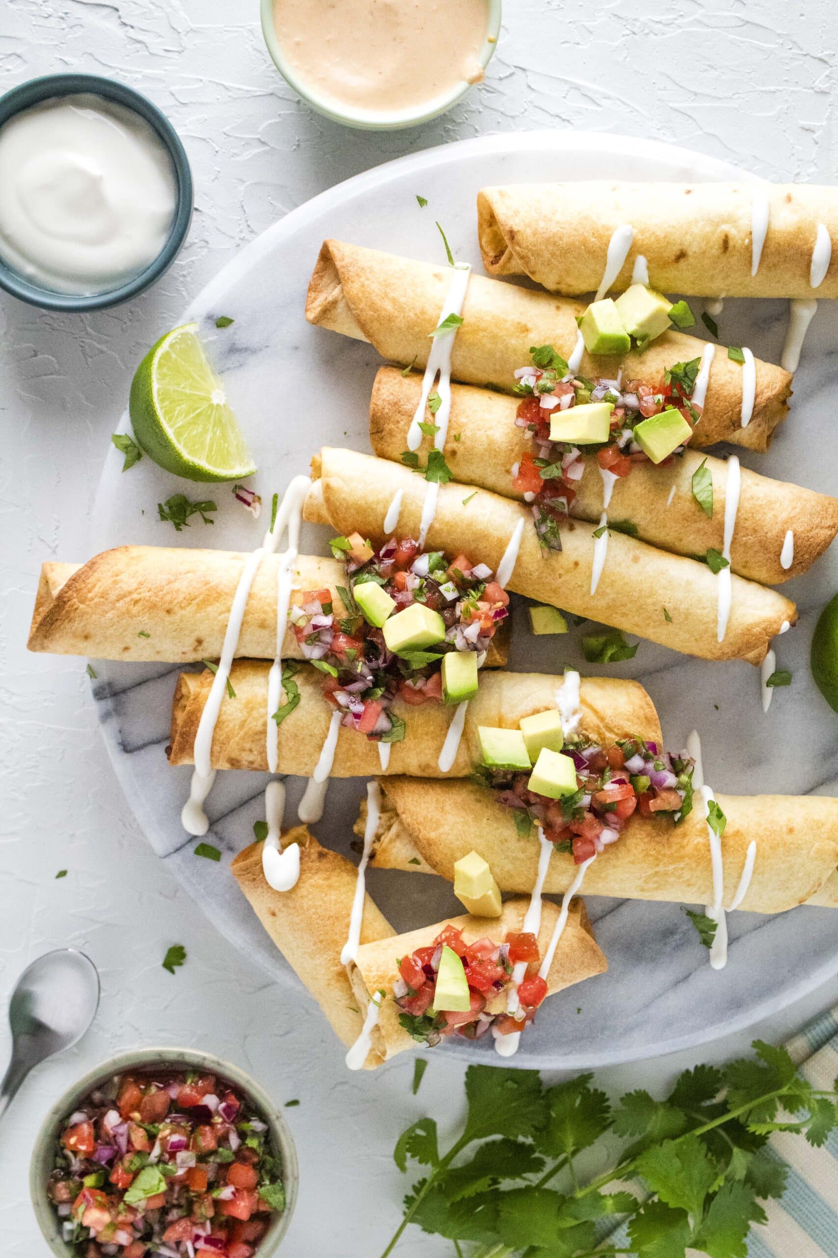 Overhead shot of air fryer taquitos on a marble lazy Susan surrounded by various toppings.