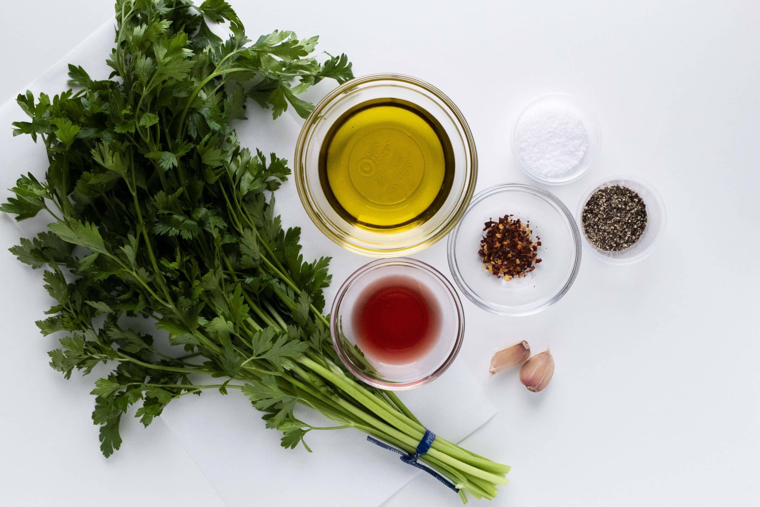 Ingredients for green chimichurri sauce on a white background.