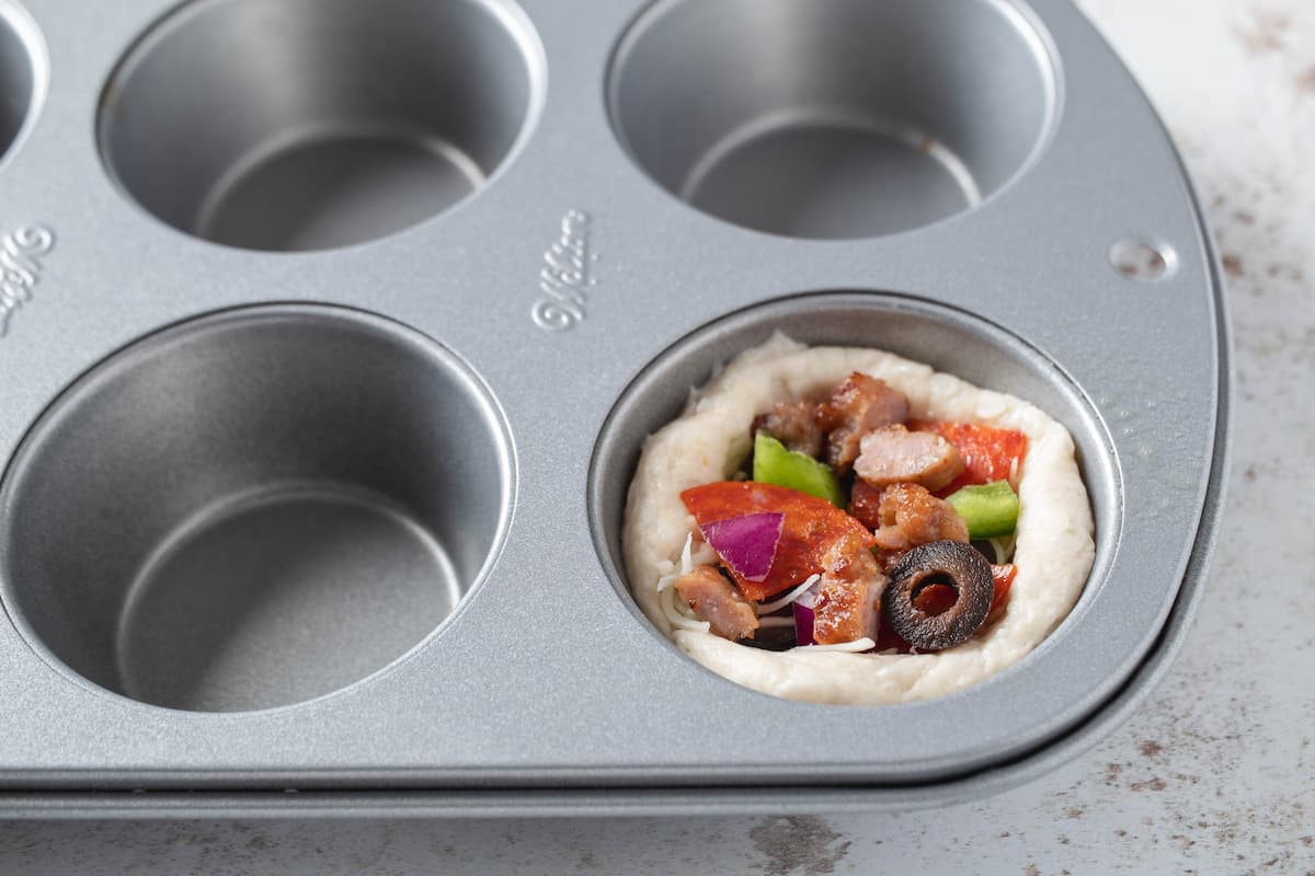 Toppings put on biscuit cups in muffin tin.