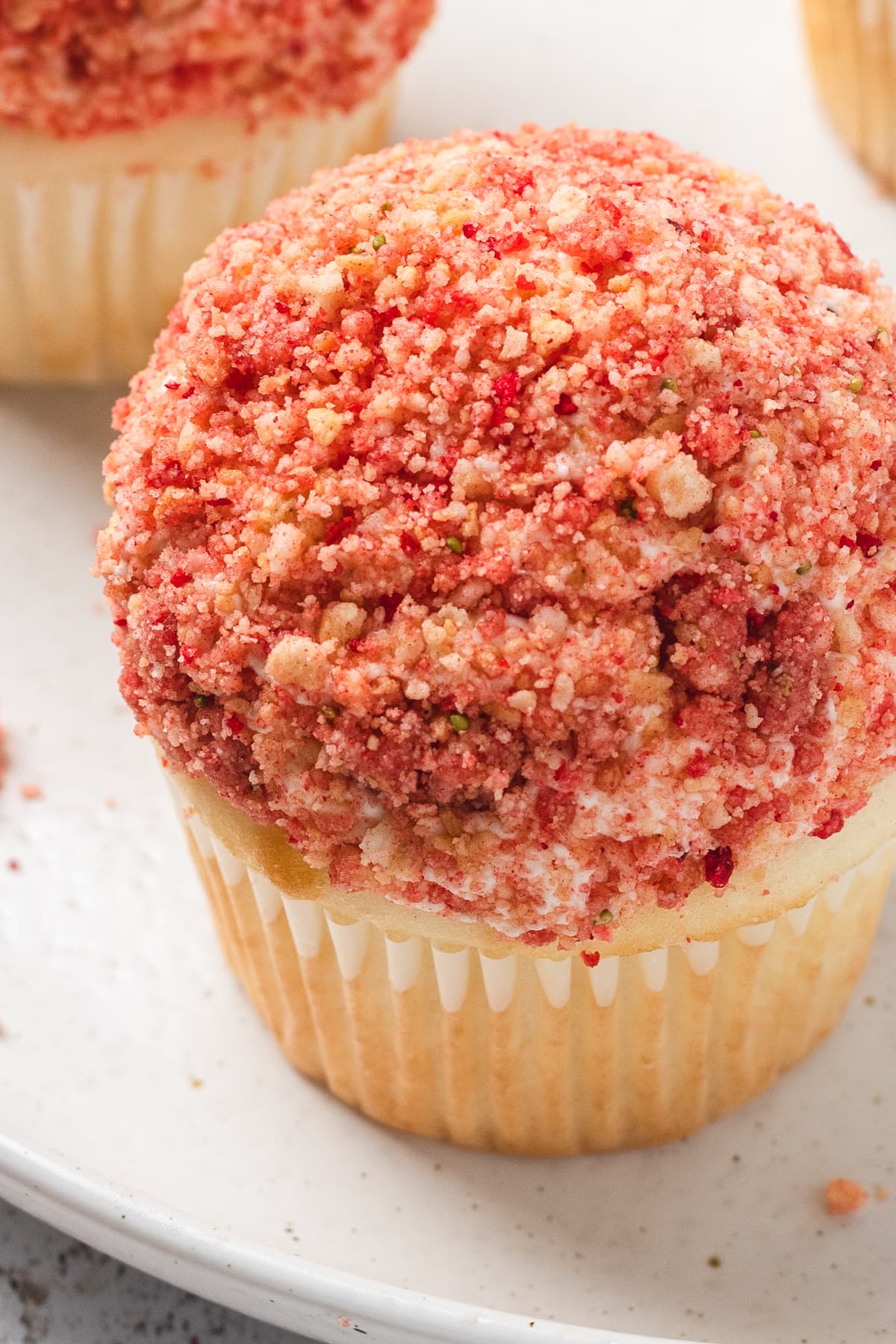 Close-up of a single strawberry crunch cupcake with crumb topping on a white plate.