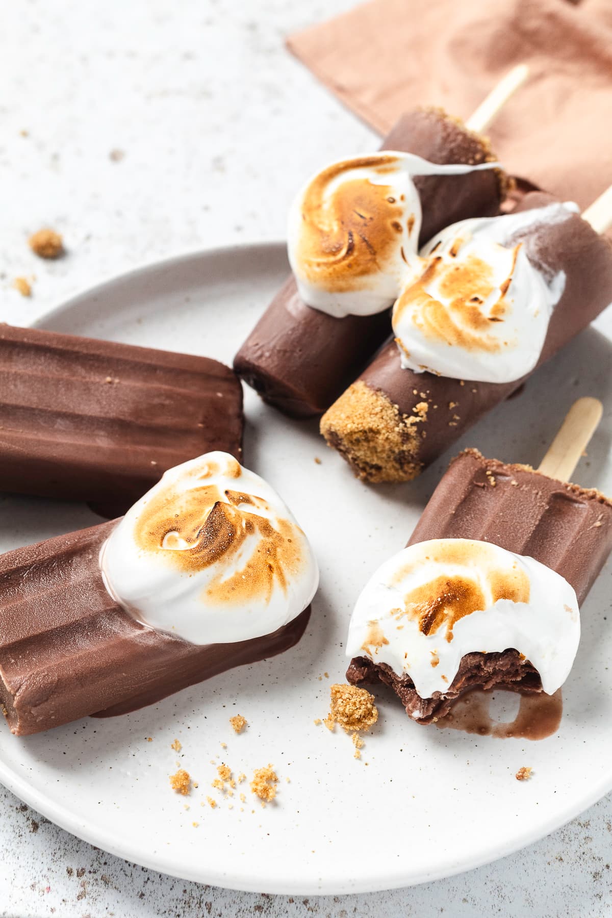 S'mores popsicles with toasted marshmallows on a light colored plate.