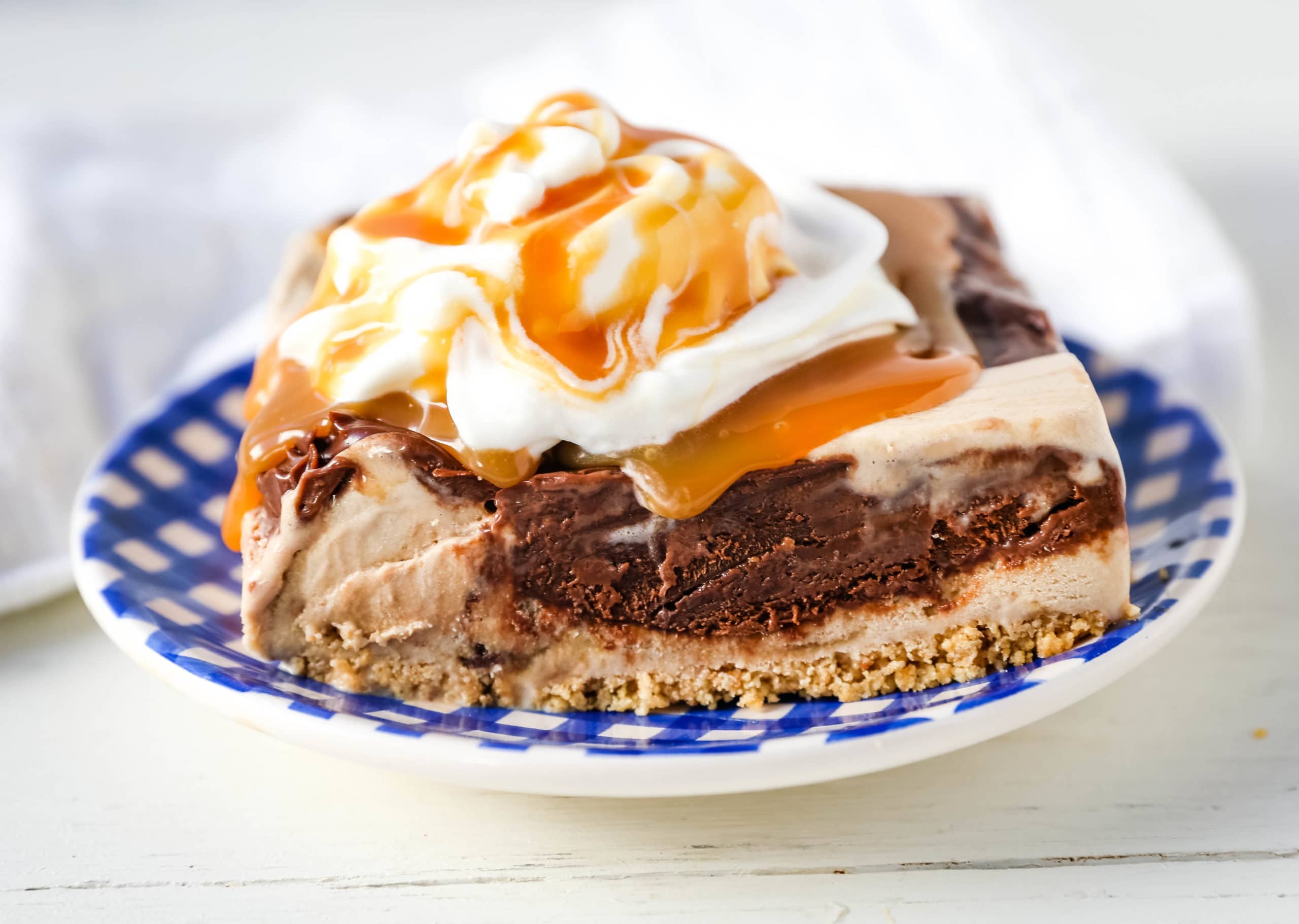 A no-bake layered dessert with ice cream, chocolate, caramel drizzle, and whipped cream on top.