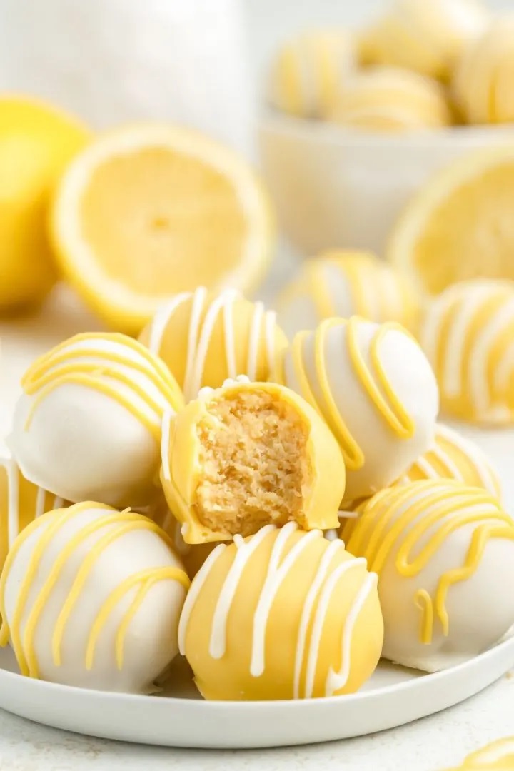 White and yellow chocolate-coated lemon truffles with a drizzle, one with a bite taken out.