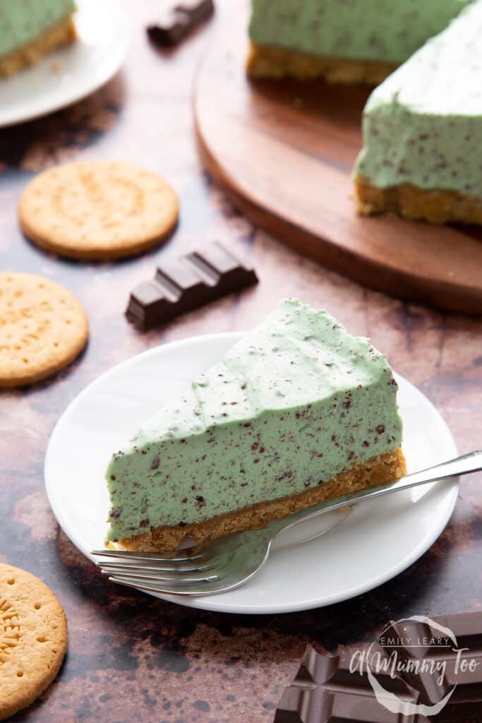 A slice of mint chocolate chip cheesecake with a biscuit crust, served on a white plate.