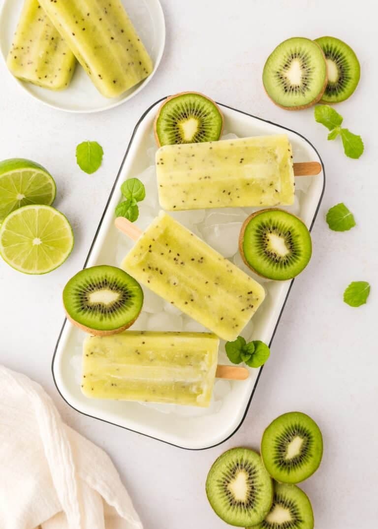 Refreshing kiwi and lime popsicles on a tray with fresh kiwi slices and mint leaves.