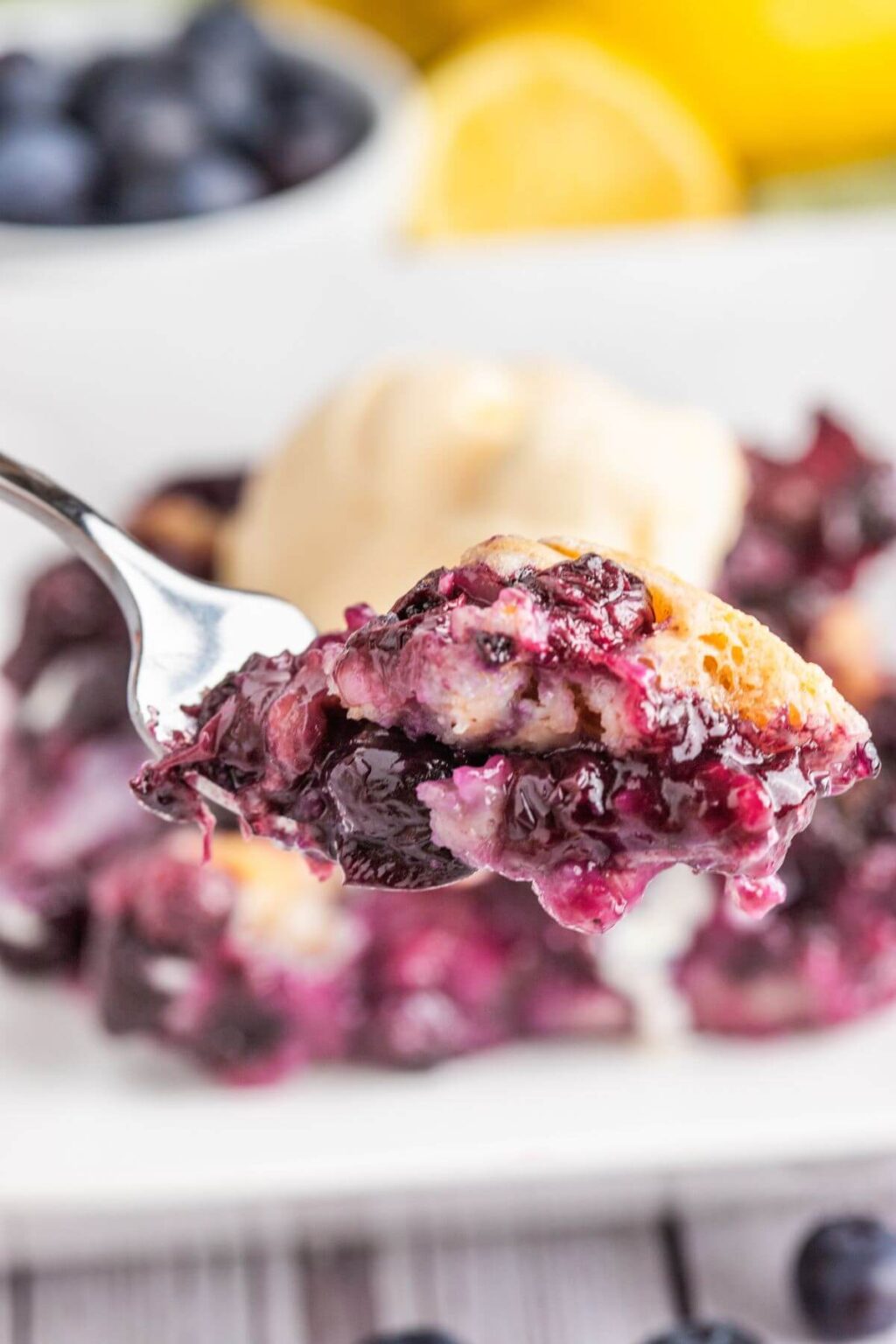 Spoonful of blueberry cobbler with juicy berries and biscuit topping, served with vanilla ice cream.