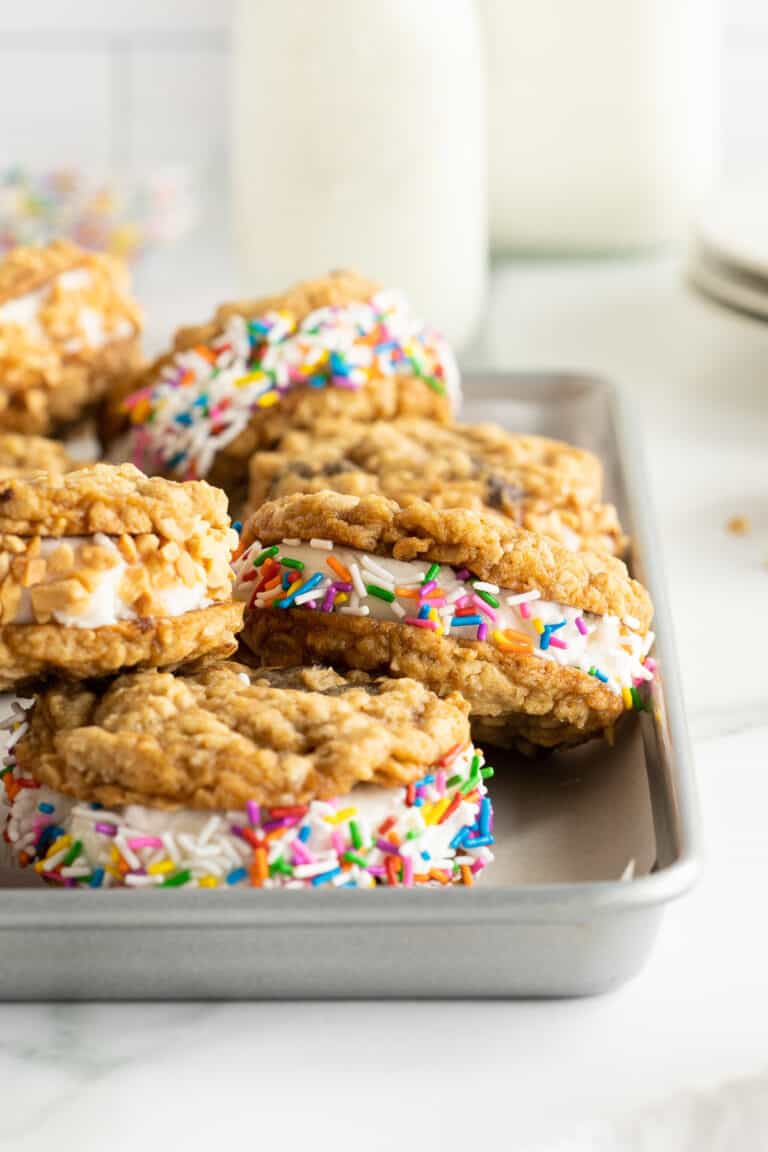 Oatmeal cookie ice cream sandwiches rolled in sprinkles and chopped nuts on a tray.


