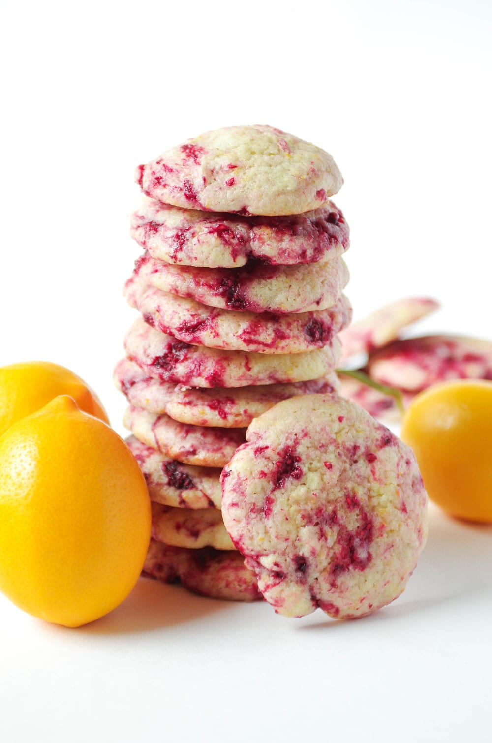 A stack of soft lemon raspberry cookies with vibrant red raspberry swirls, surrounded by fresh lemons.