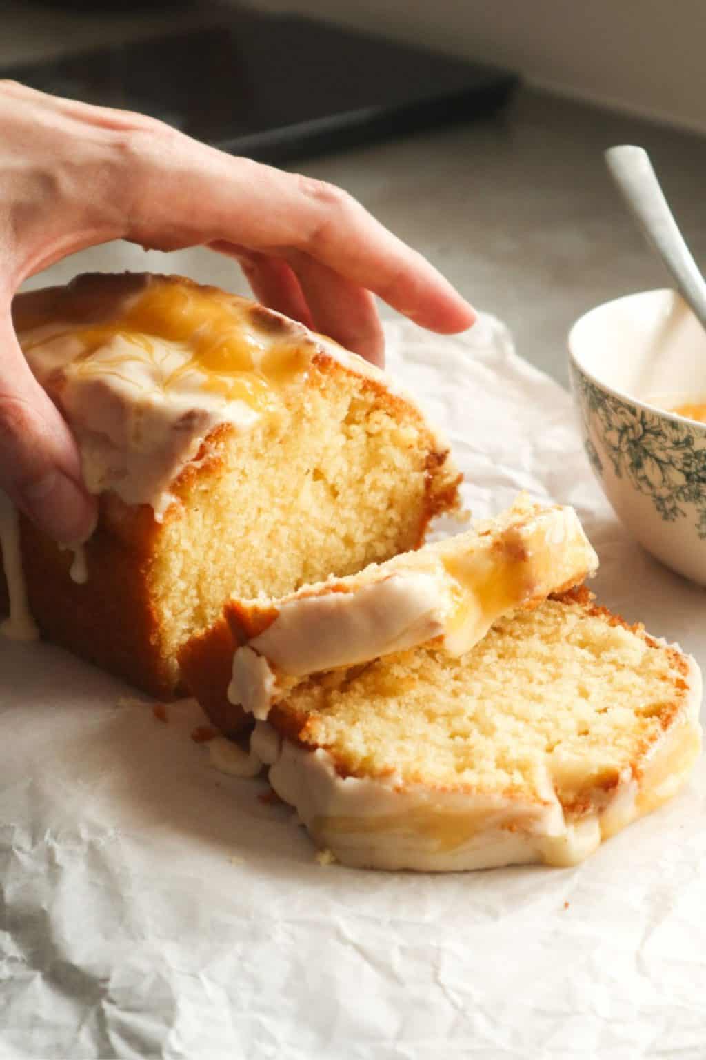 Lemon pound cake with a lemon glaze and curd, with a hand slicing a piece.