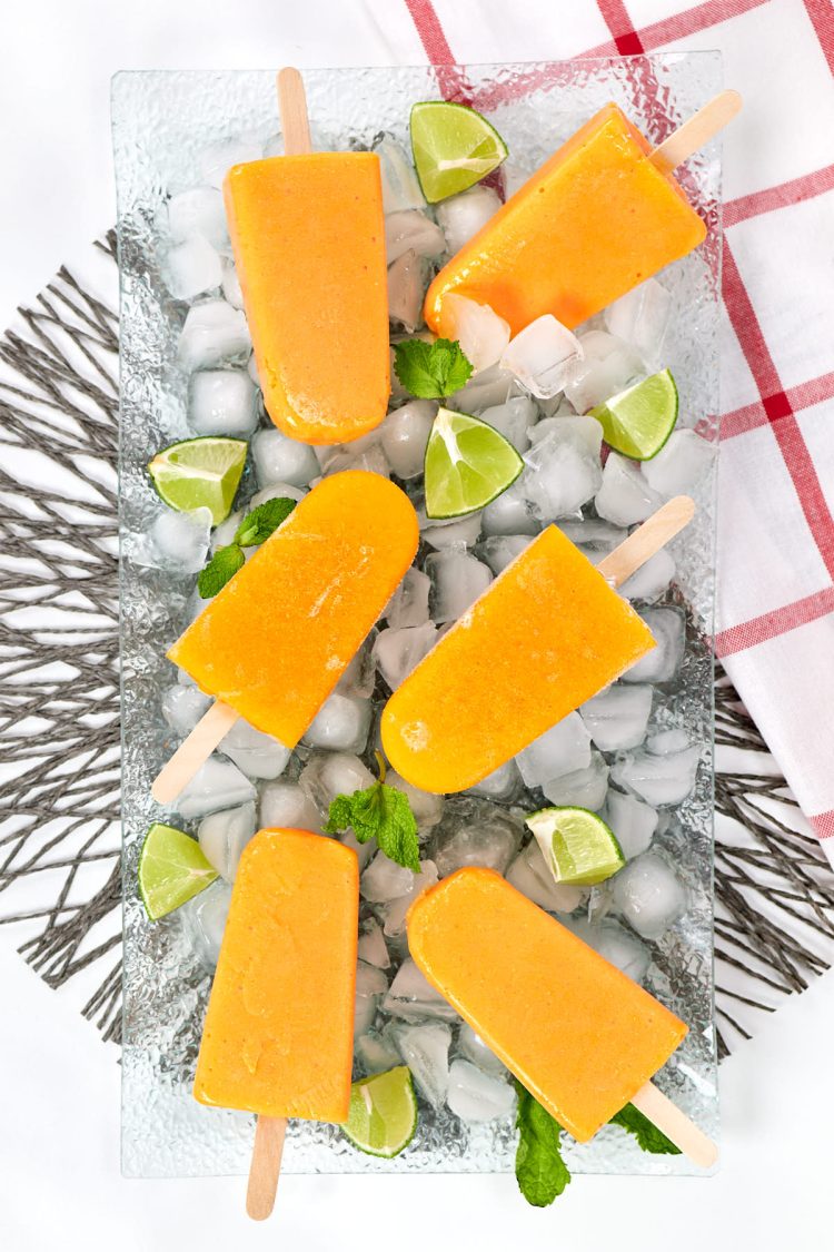 Mango popsicles on ice with lime wedges and mint leaves.