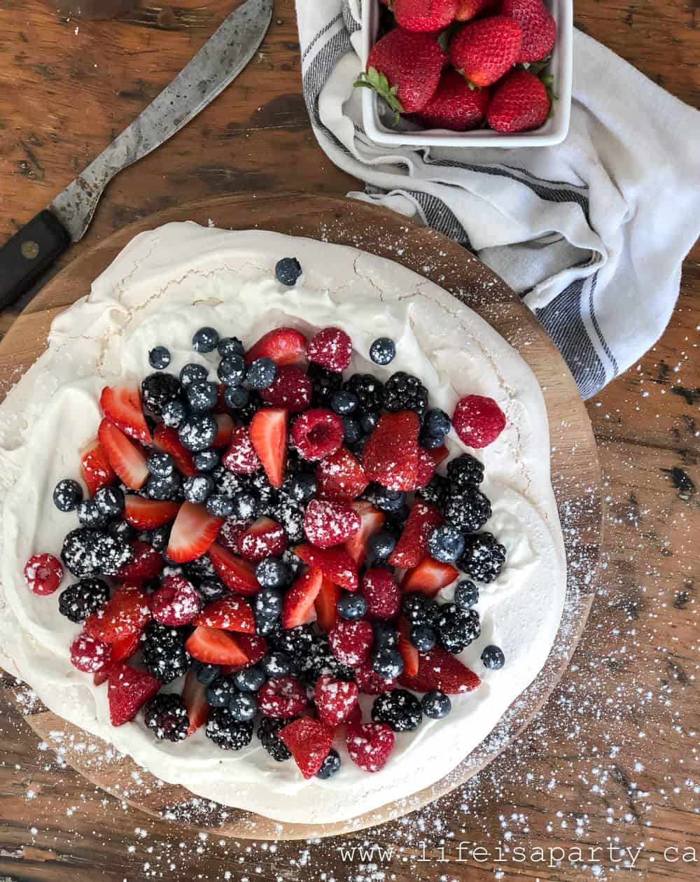 Pavlova topped with strawberries, blueberries, blackberries, and raspberries, dusted with powdered sugar.