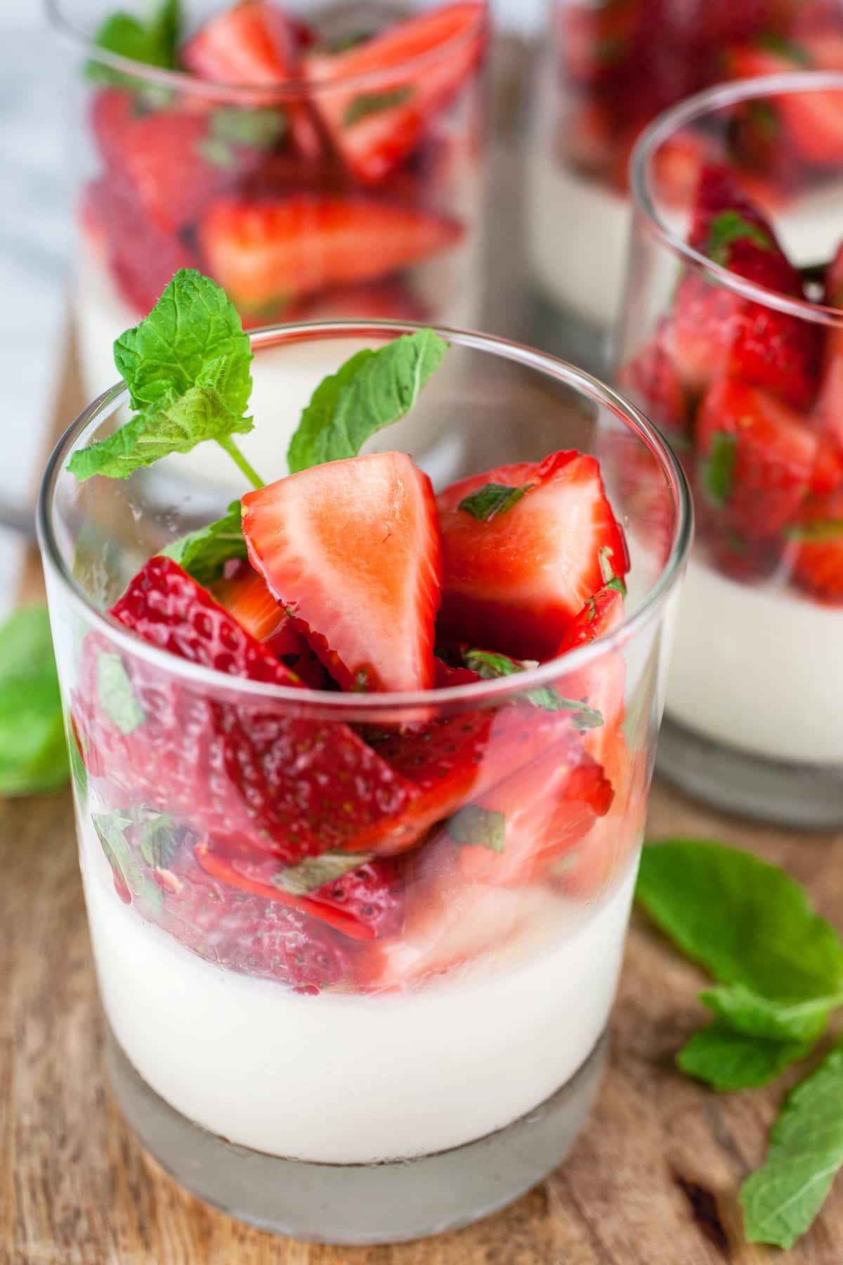 A glass of strawberry mint panna cotta with fresh strawberries and mint leaves on top.