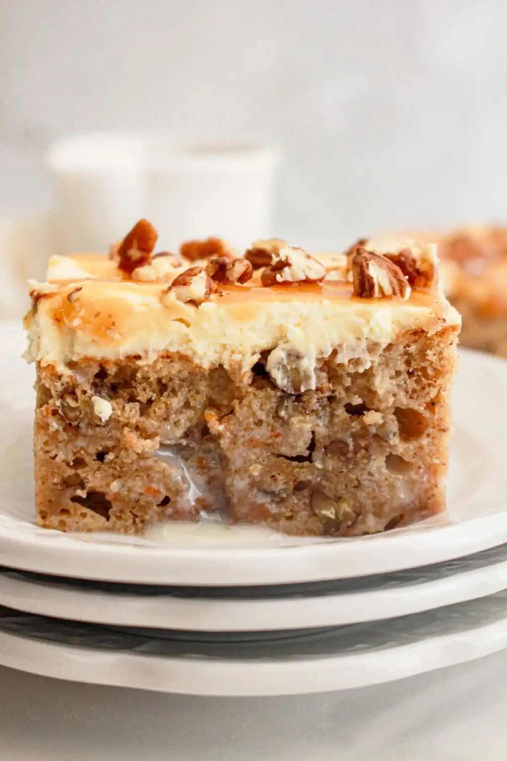 A slice of carrot cake poke cake with cream cheese frosting, topped with pecans and caramel drizzle.