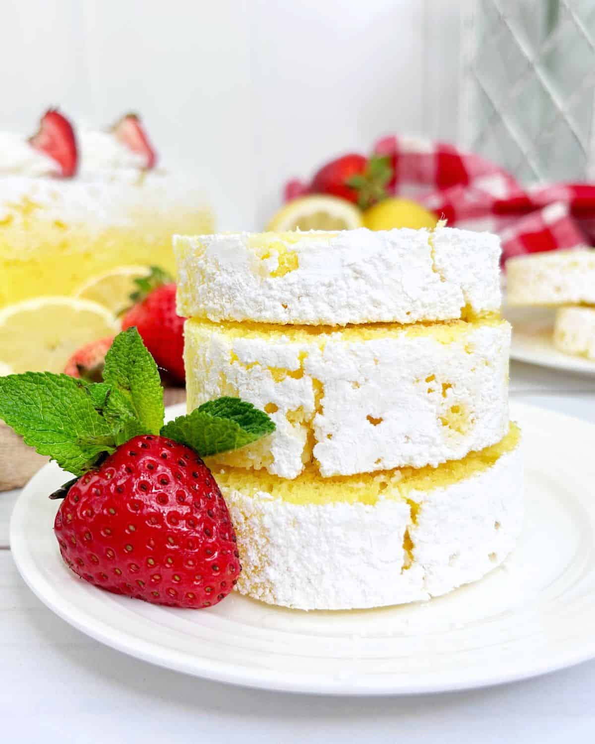 A sliced lemon cake roll with a dusting of powdered sugar, stacked neatly with a fresh strawberry and mint garnish.