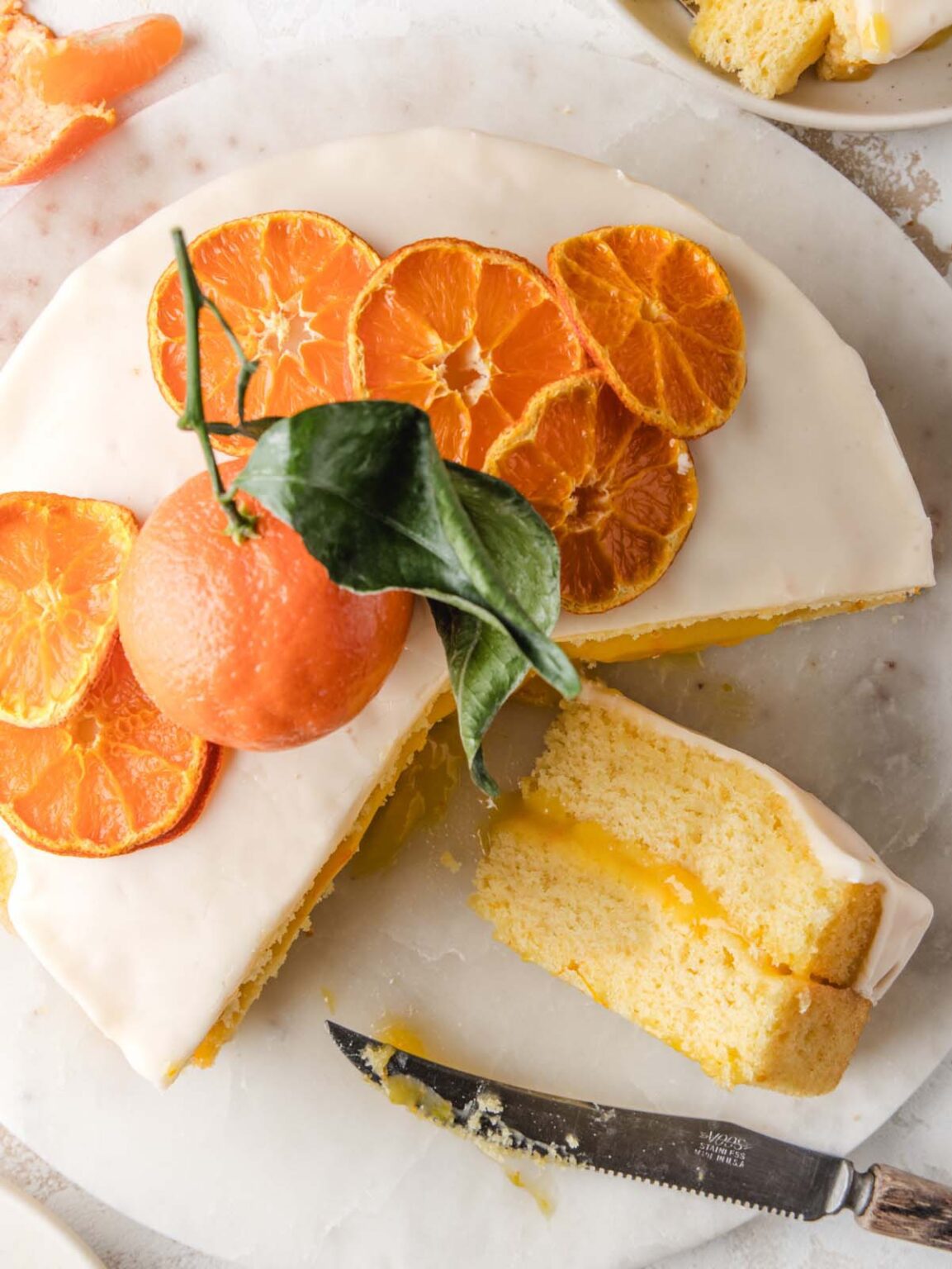A mandarin orange cake with a smooth glaze, topped with dried orange slices and a whole mandarin with leaves.