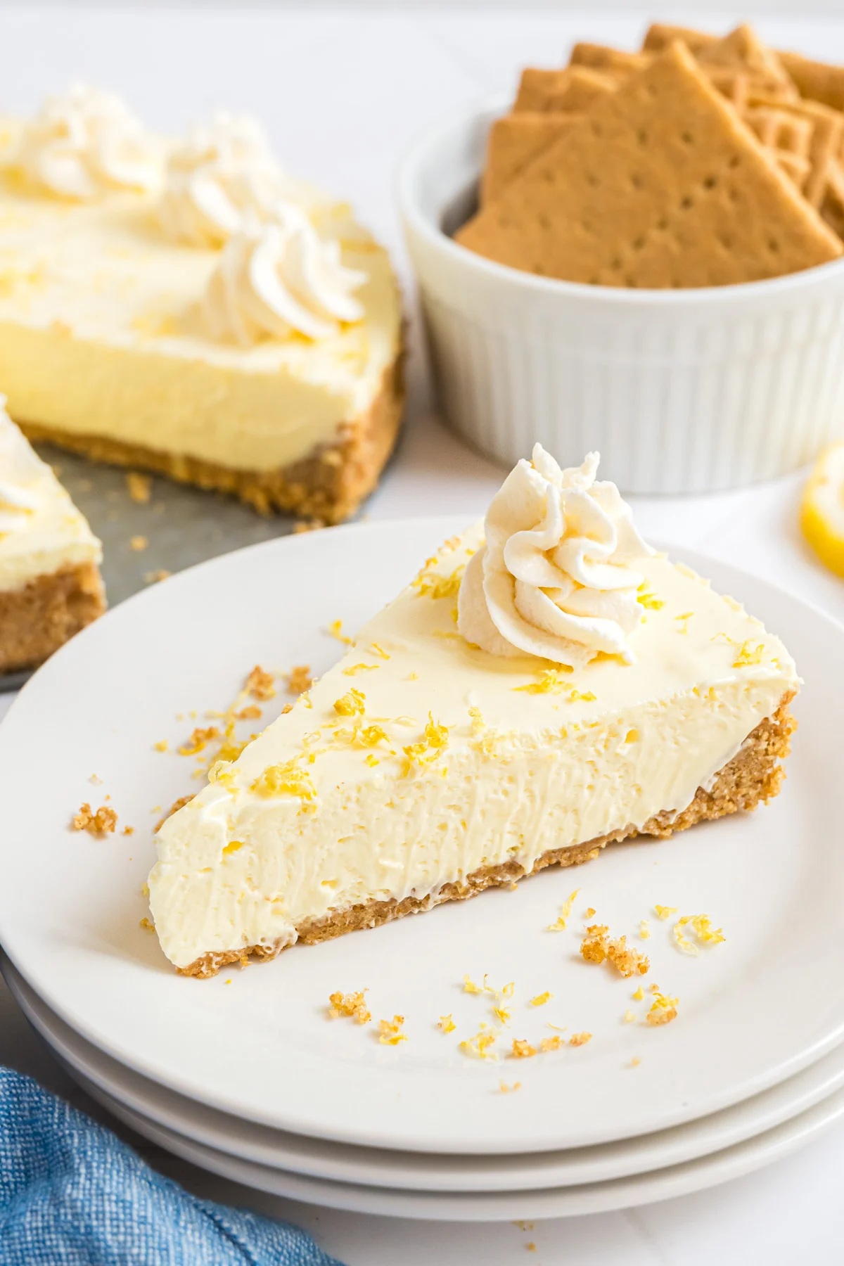 A slice of no-bake lemon cheesecake on a graham cracker crust, topped with whipped cream and lemon zest.