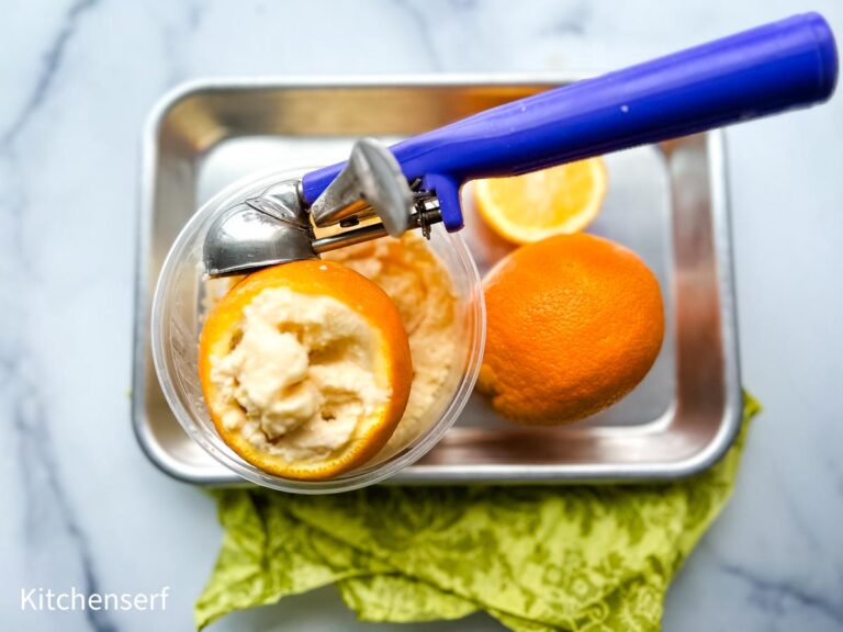 No-churn orange sherbet served in a hollowed orange peel with an ice cream scooper.