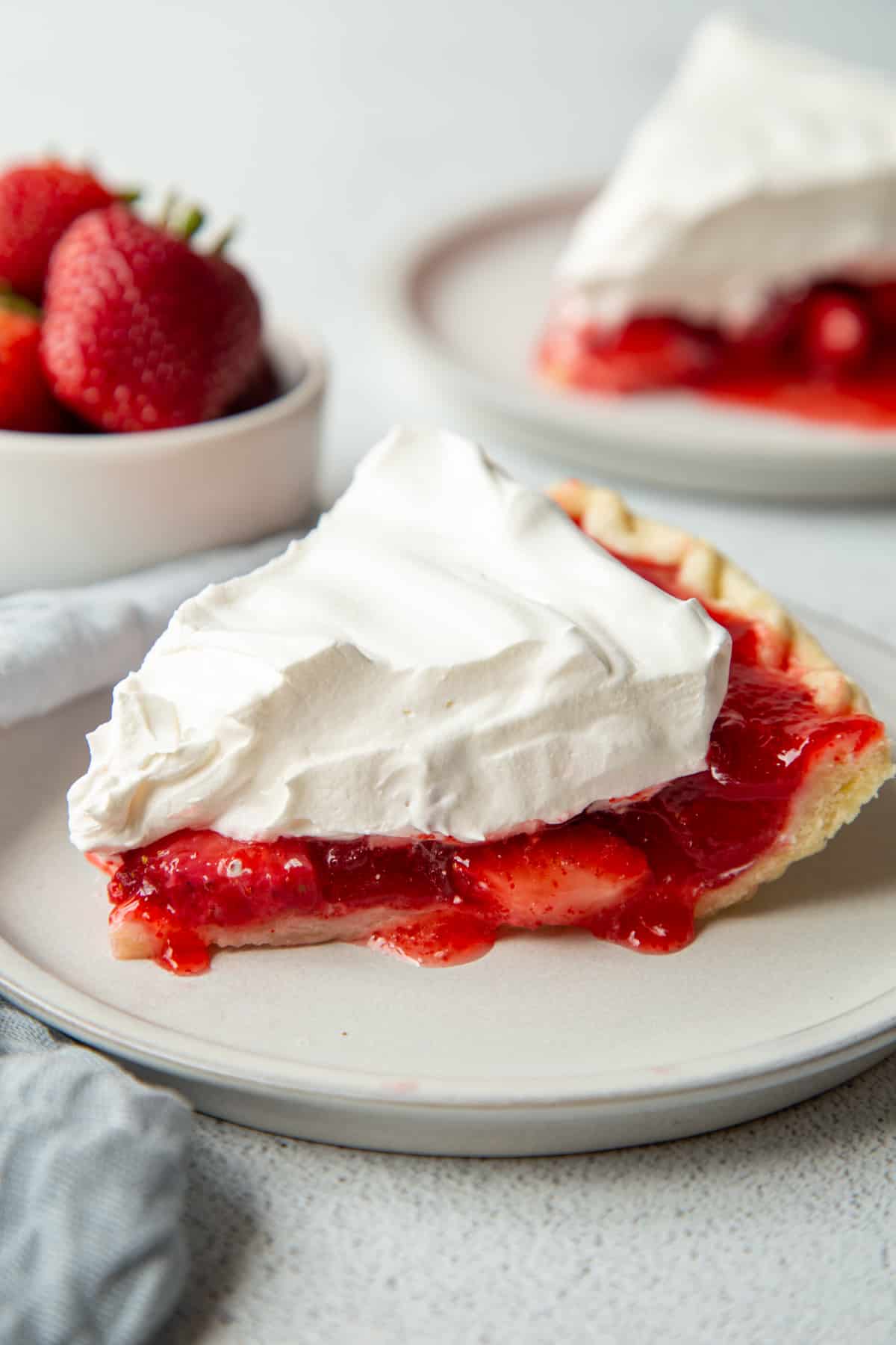 A slice of strawberry jello pie with a flaky crust, red strawberry filling, and a thick whipped cream topping.