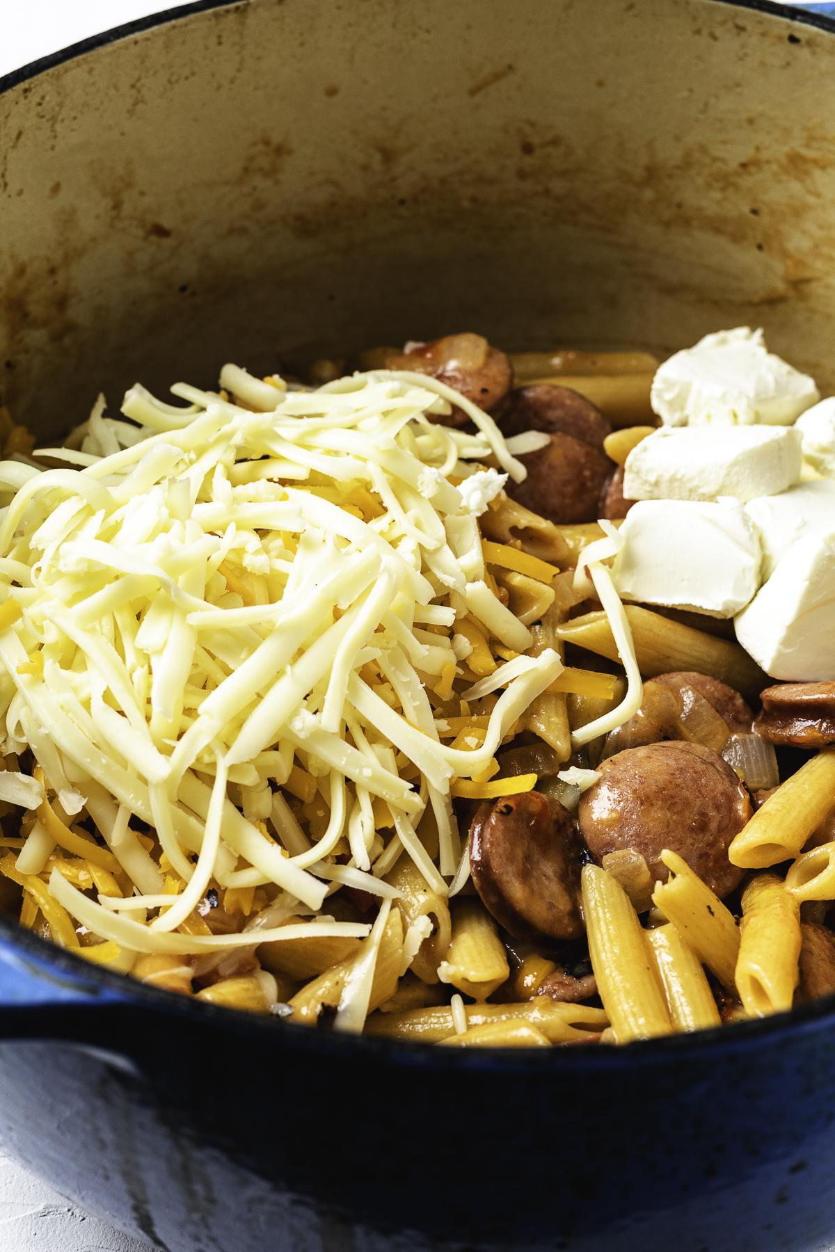 Shredded cheese and cream cheese added to cooked kielbasa and pasta in a large Dutch oven.