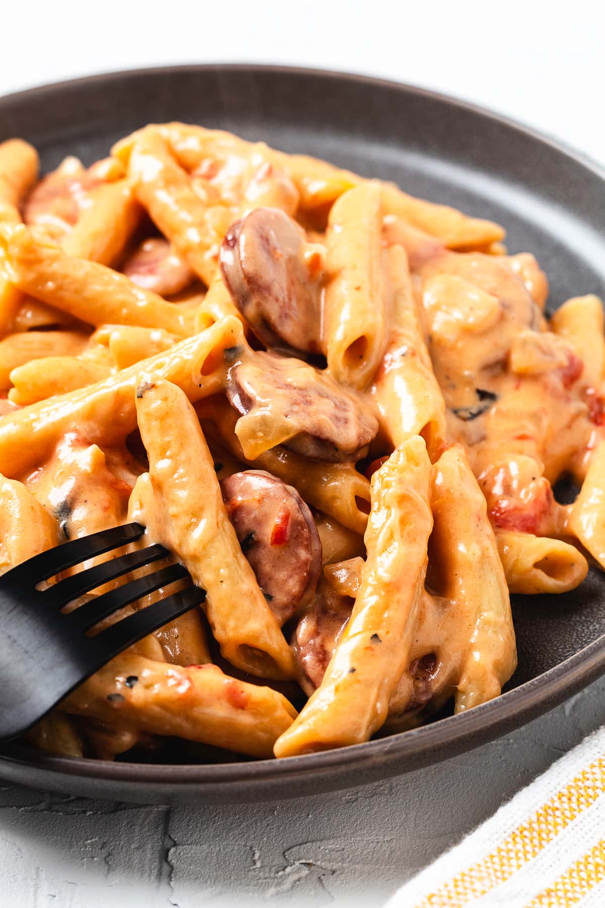 Close-up of creamy cheesy kielbasa pasta served on a dark plate with a black fork.