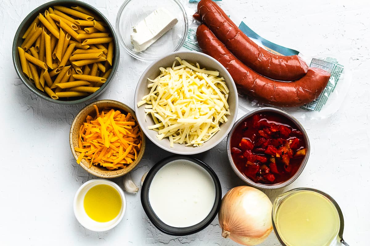 Ingredients for cheesy kielbasa pasta including pasta, sausage, cheese, onion, broth, and cream.
