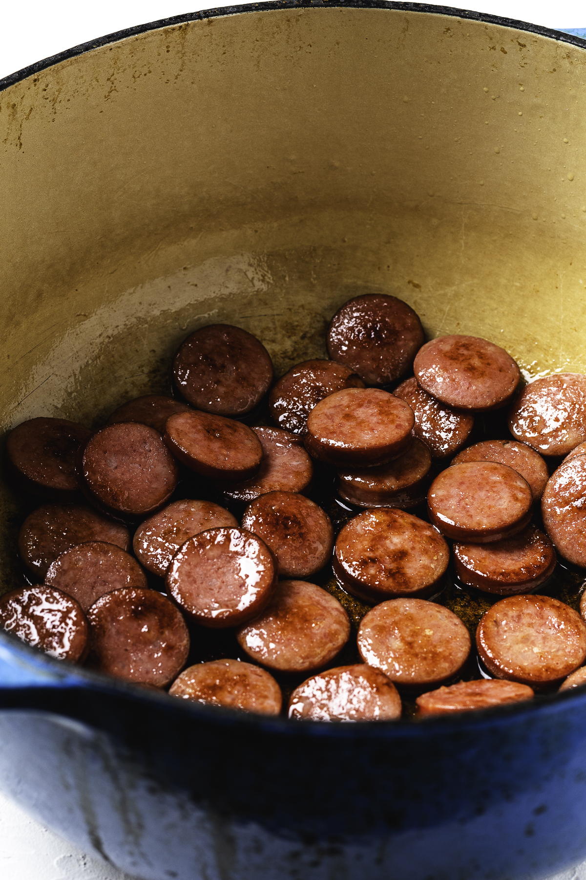 Sliced kielbasa browning in a large blue Dutch oven.