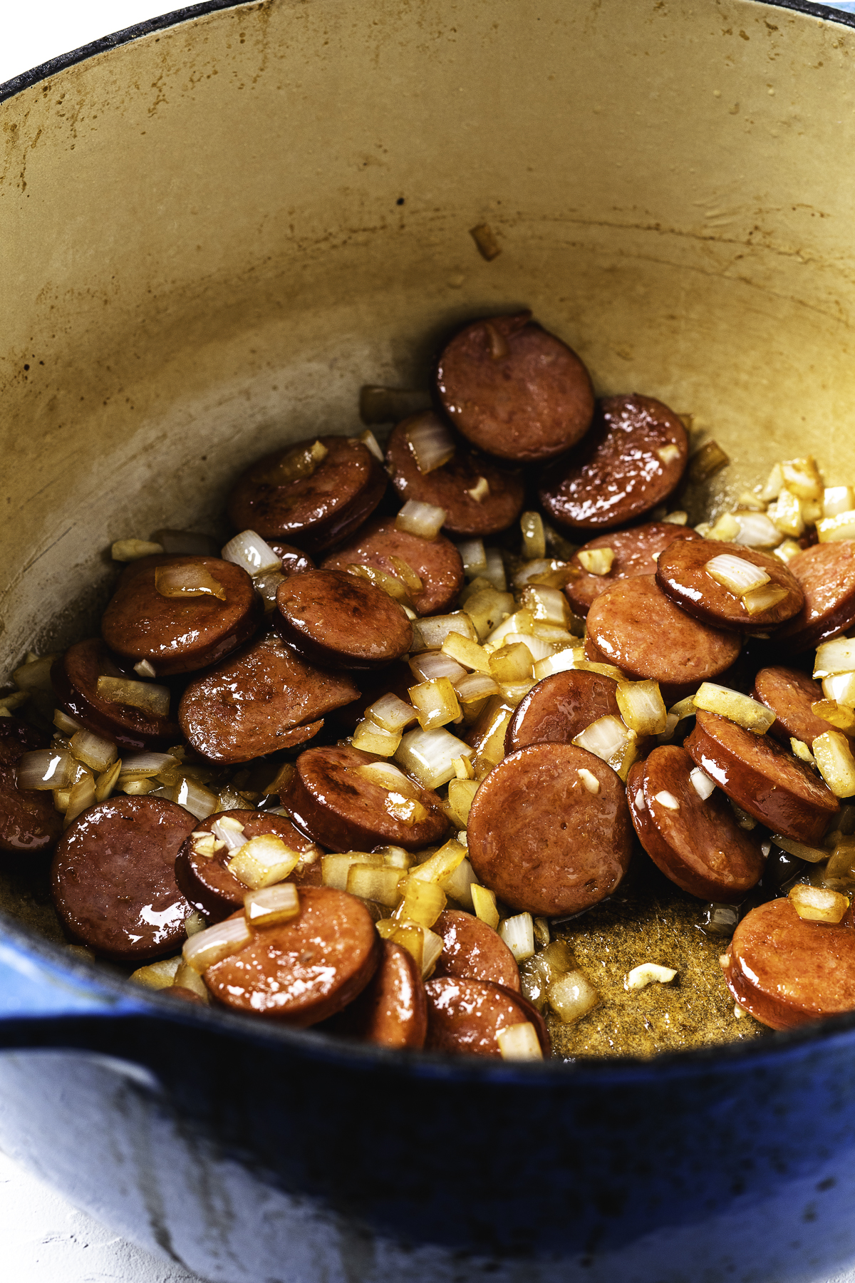 Sautéed kielbasa and onions cooking together in a Dutch oven.