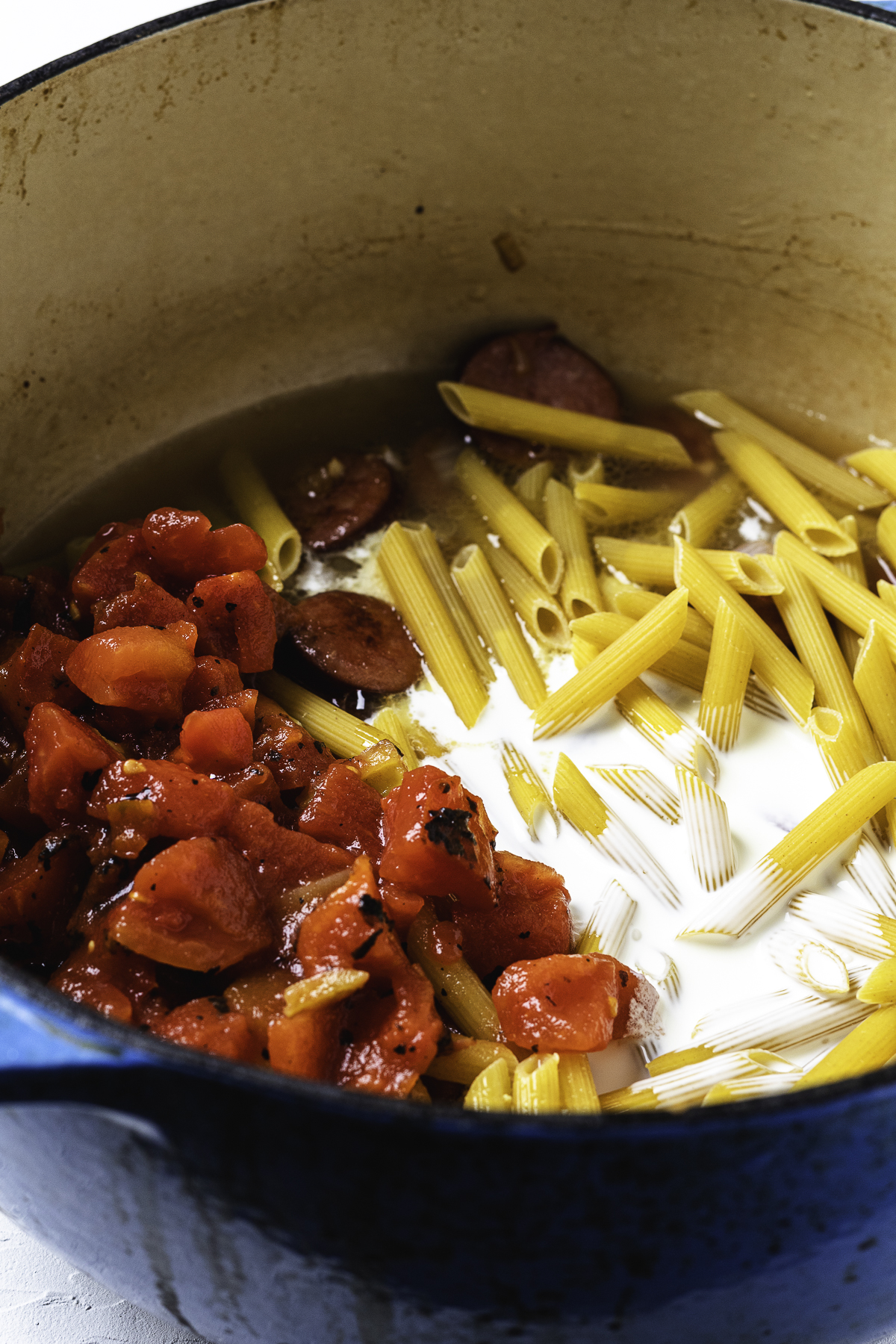 Uncooked pasta, diced tomatoes, kielbasa, and cream in a Dutch oven before mixing.

