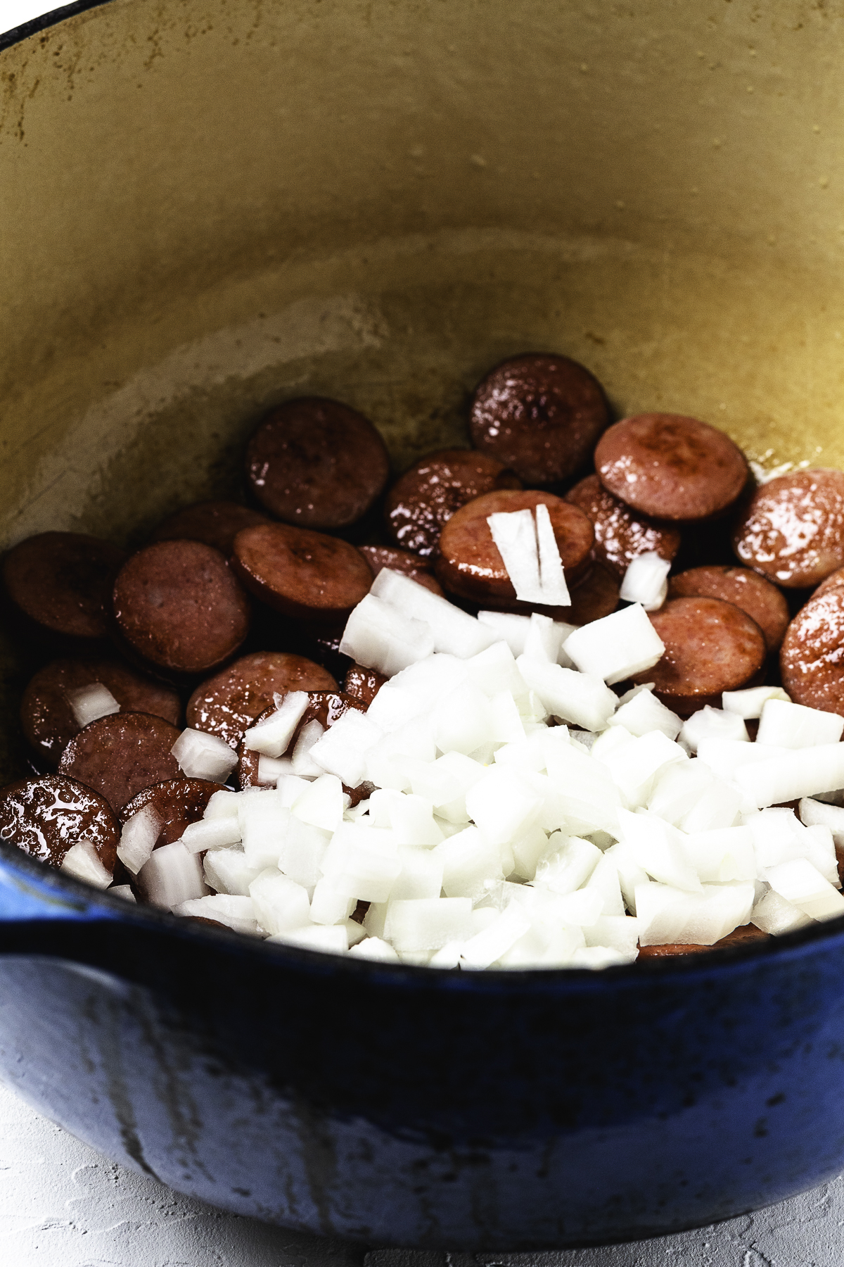 Diced onions added to sliced kielbasa cooking in a large Dutch oven.