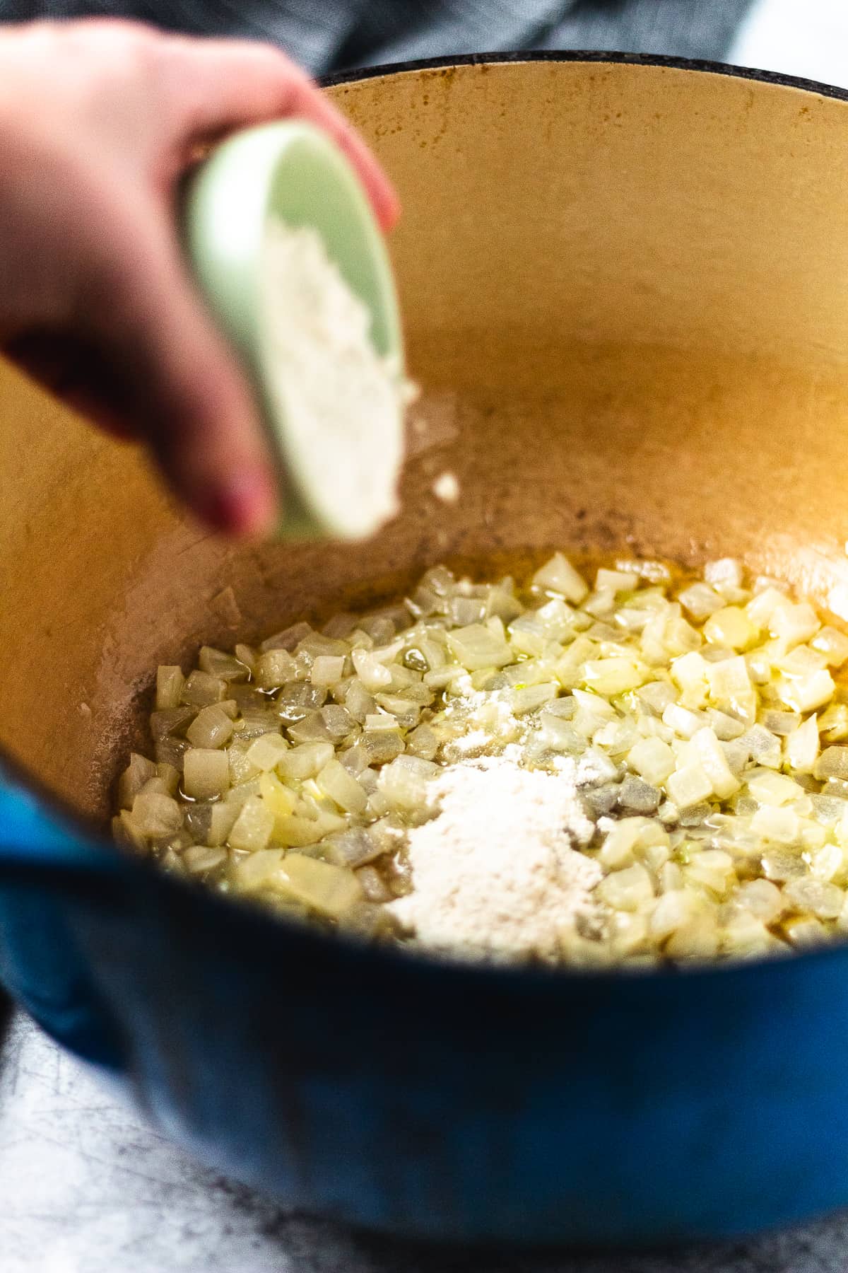 Sautéed onions in a Dutch oven with flour being added from a small green bowl to start the roux.