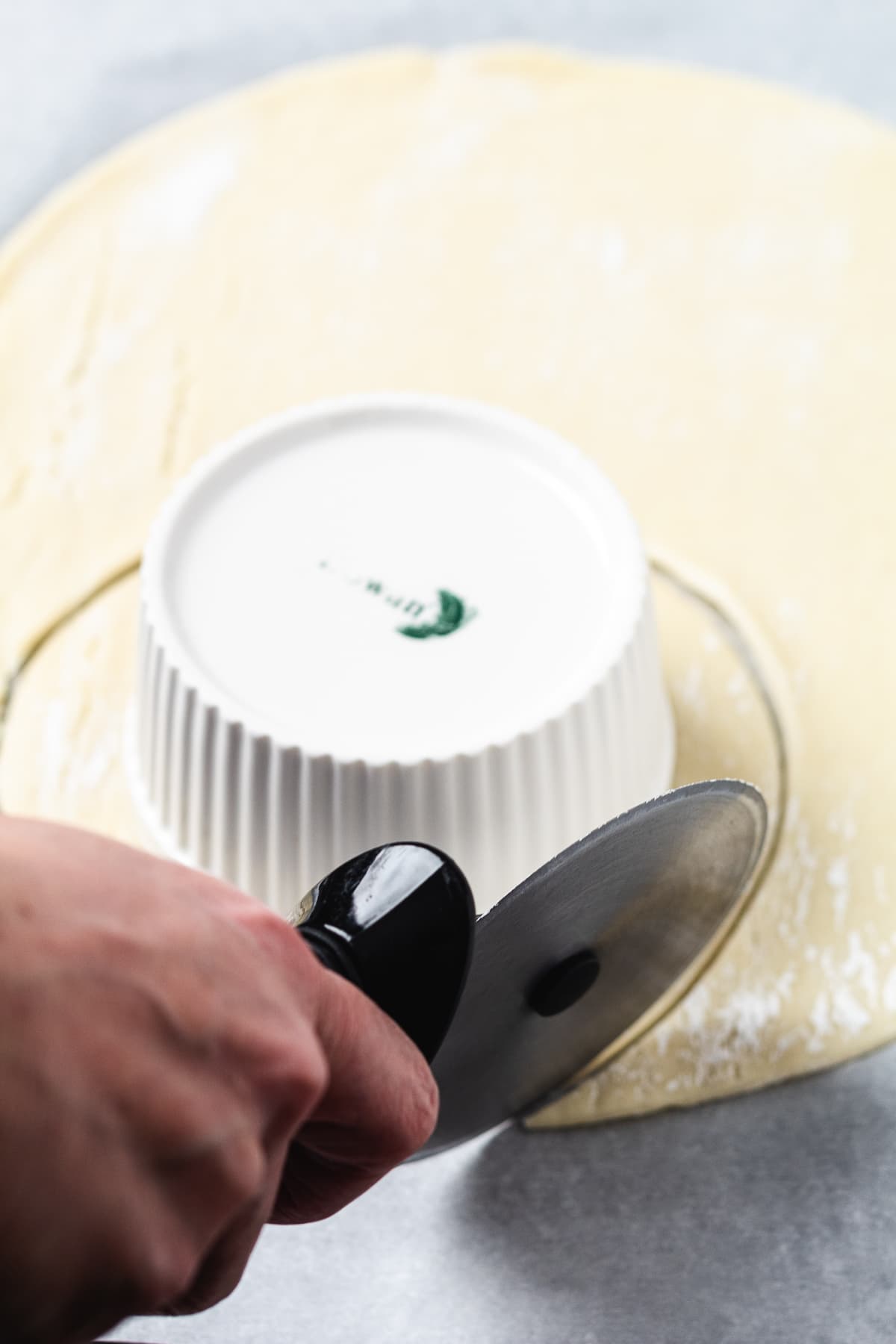 Using a pizza cutter to trim pie crust around an upside-down ramekin for chicken pot pie topping.