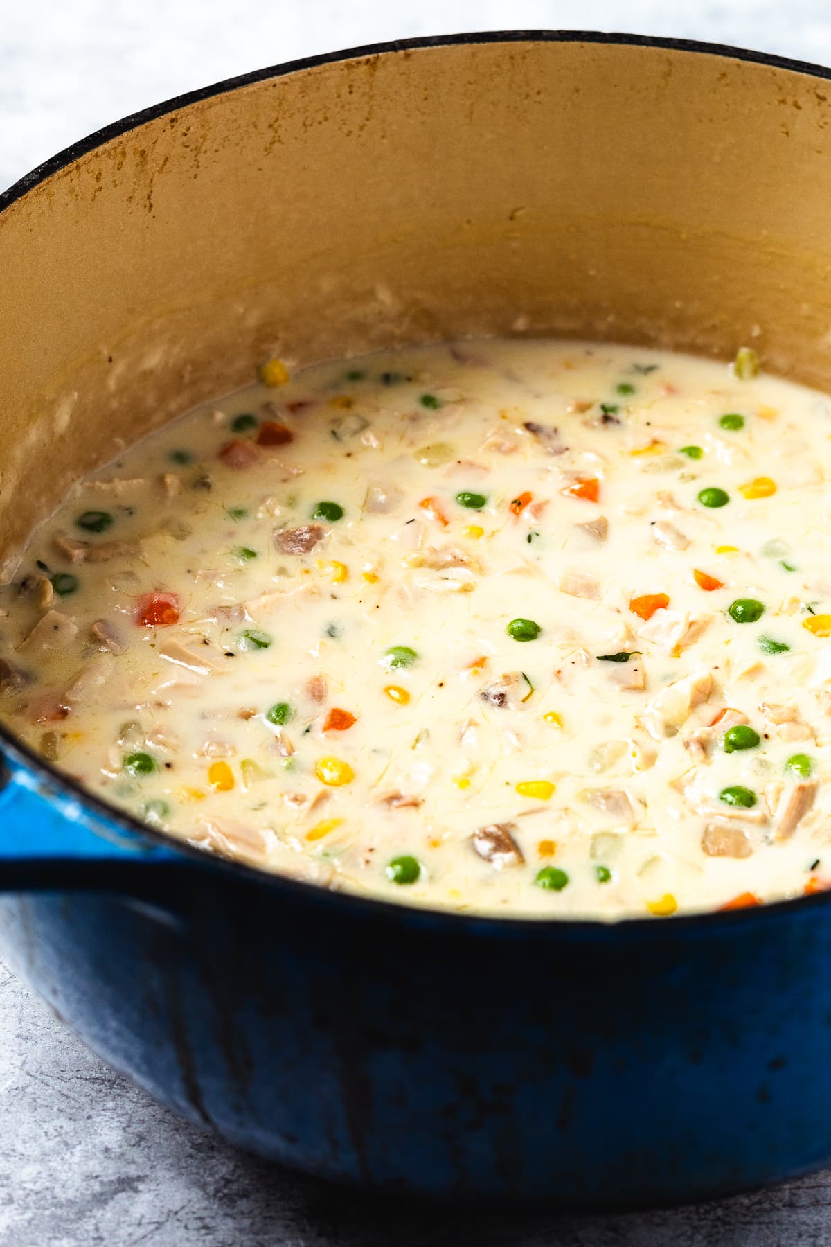 Creamy chicken pot pie filling in a blue Dutch oven with mixed vegetables and chunks of chicken.