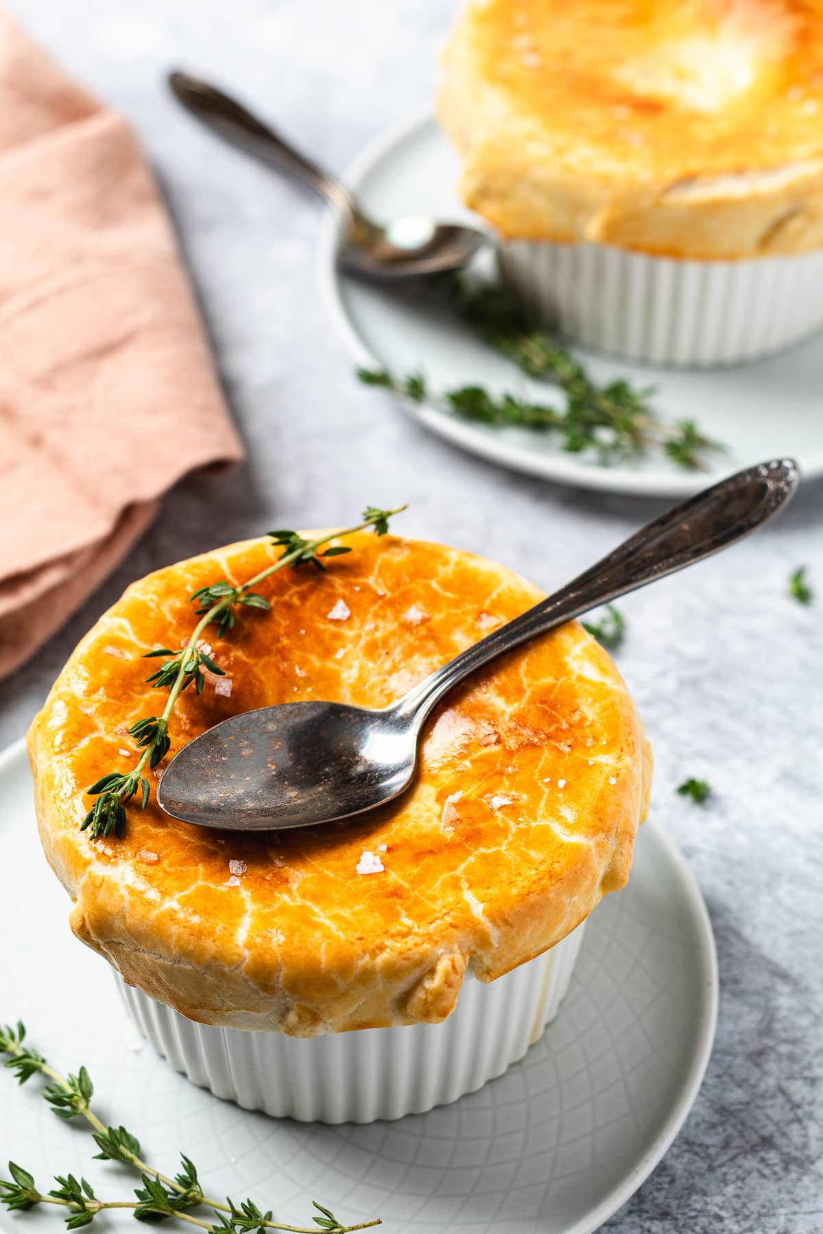 Close-up of baked chicken pot pie with flaky crust, spoon on top, and sprigs of fresh thyme.