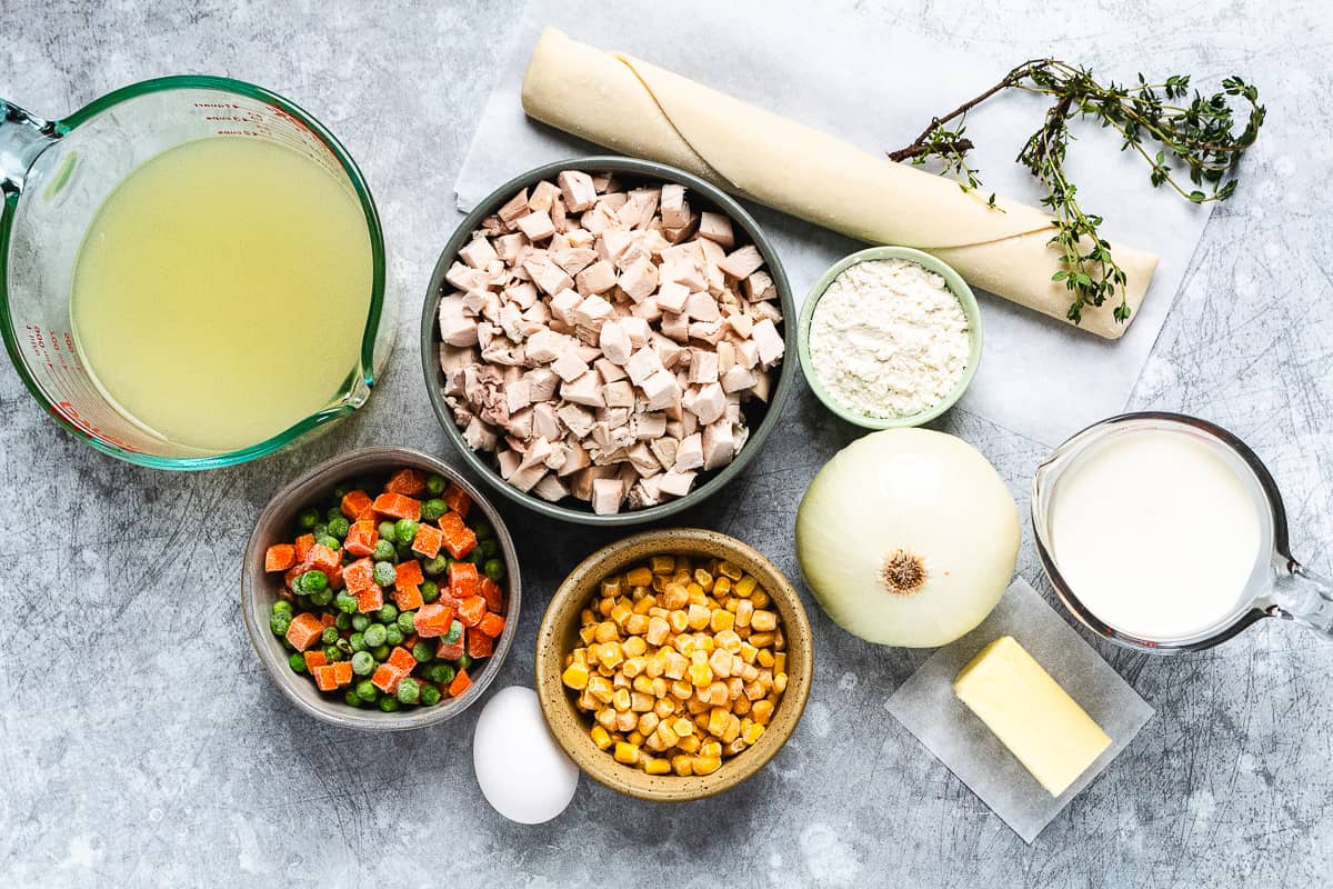 Flat lay of chicken pot pie ingredients including chicken, broth, veggies, flour, and pie crust.