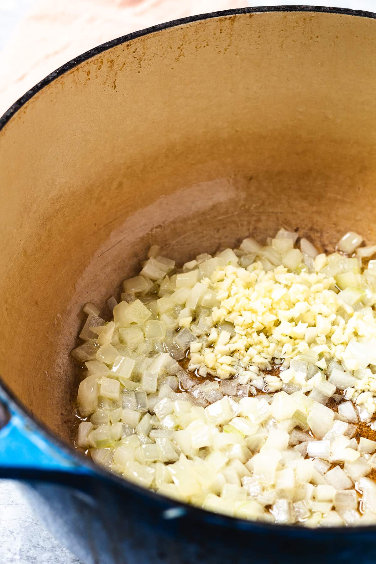 Chopped onions and garlic being sautéed in a Dutch oven with oil to start the chicken pot pie base.