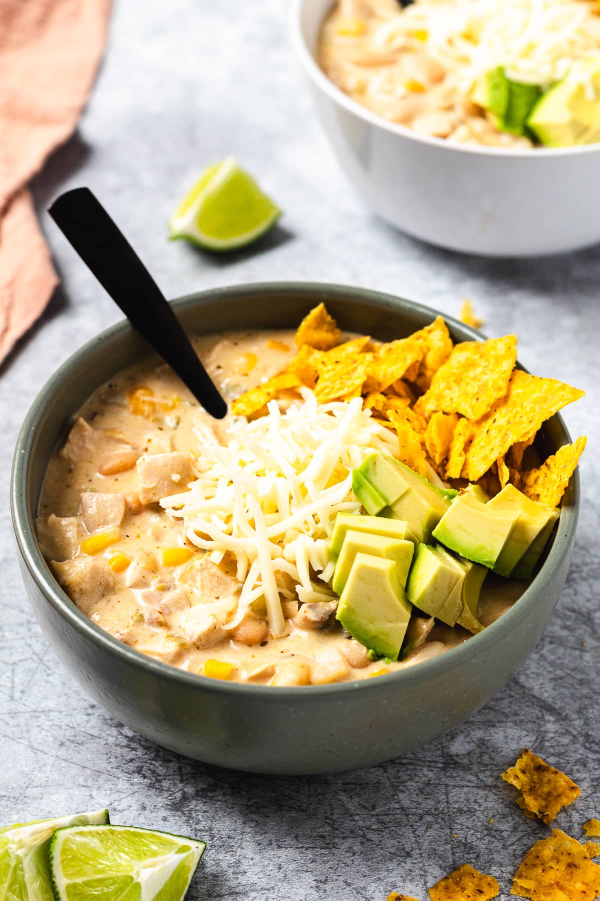 Bowl of white chicken chili topped with shredded cheese, avocado slices, and crushed tortilla chips.