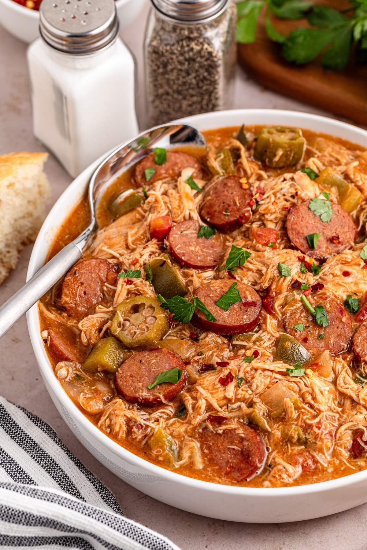 A bowl of gumbo with shredded chicken, sliced sausage, okra, and chopped vegetables.