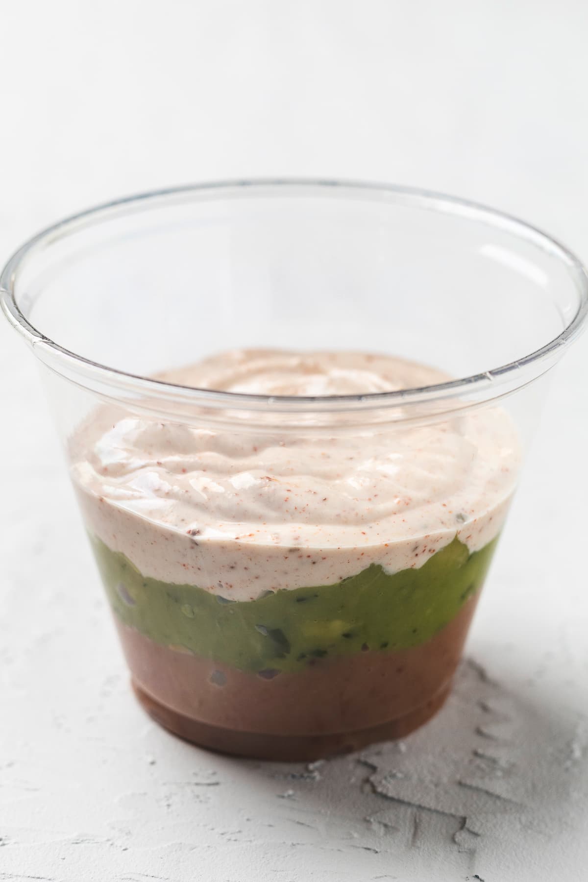 First 3 layers of taco dip layered in a clear disposable cup.