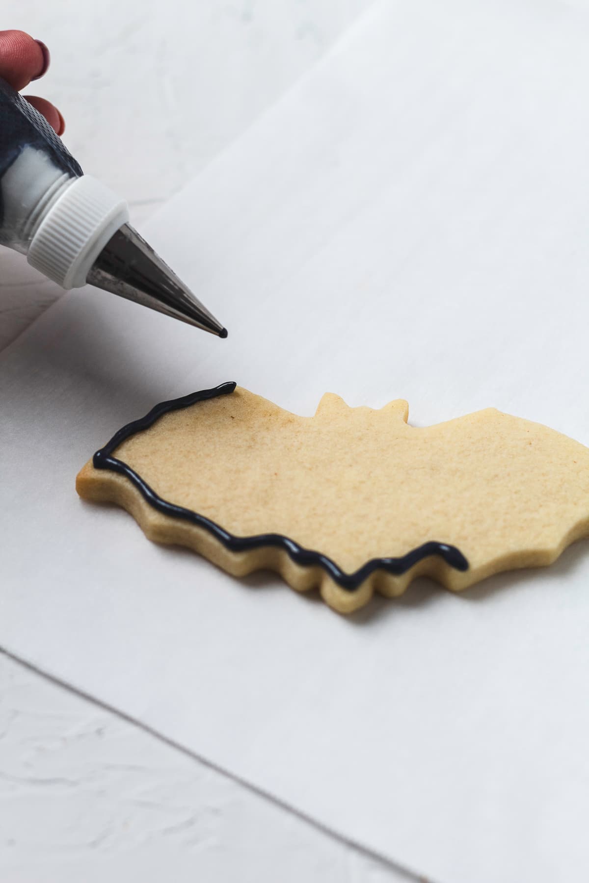 A piping bag outlines the edge of a bat-shaped sugar cookie with black royal icing.