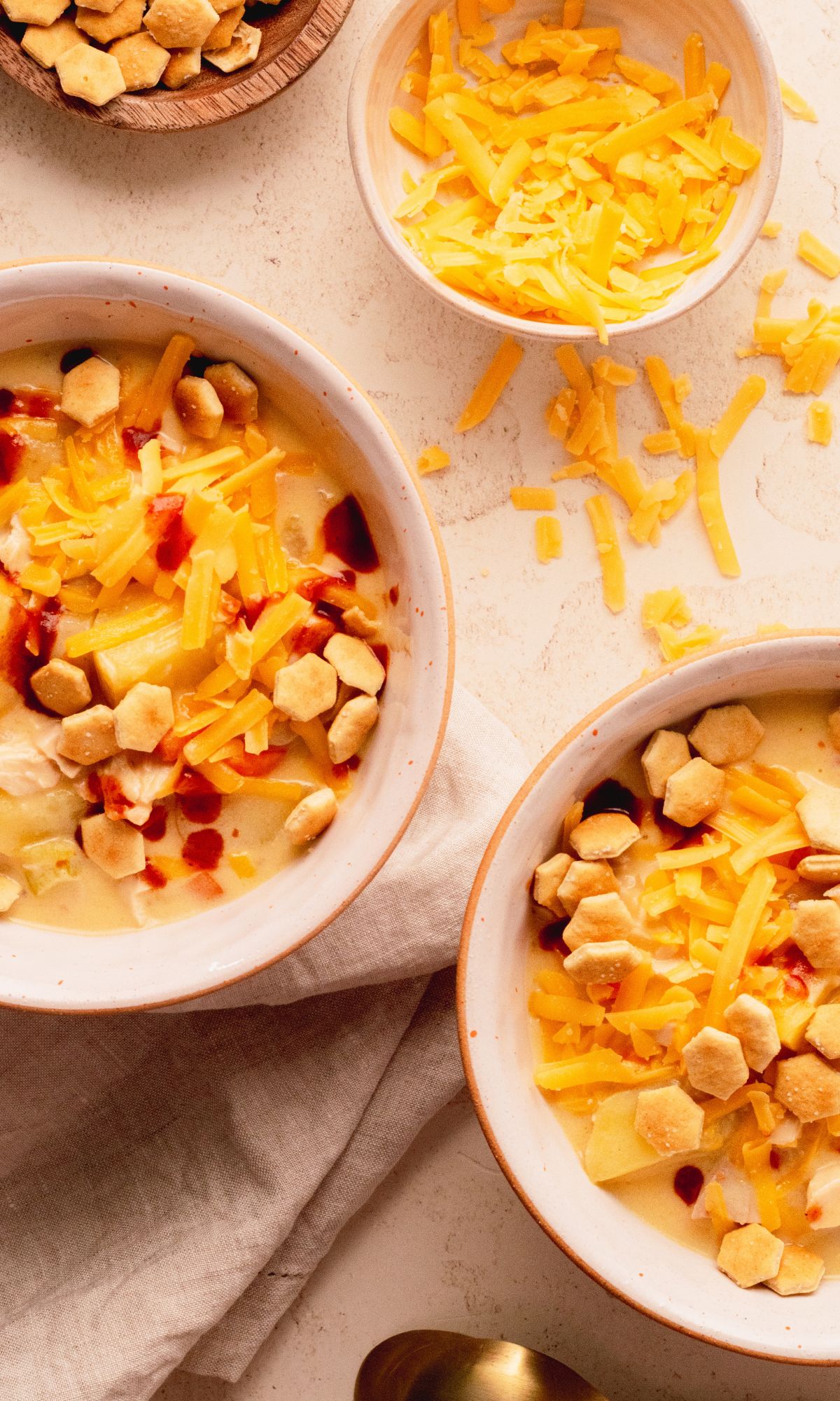 Chicken soup with cheese, vegetables, crackers, and hot sauce.