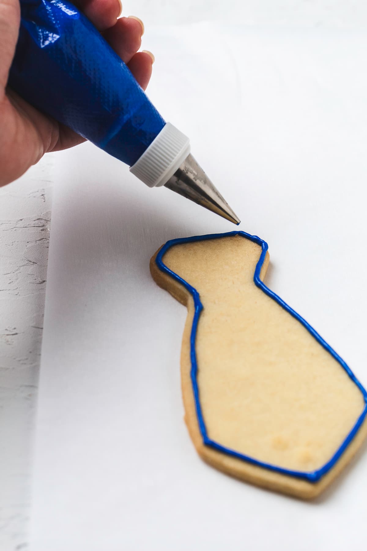 Hand outlining necktie cookie with royal icing.