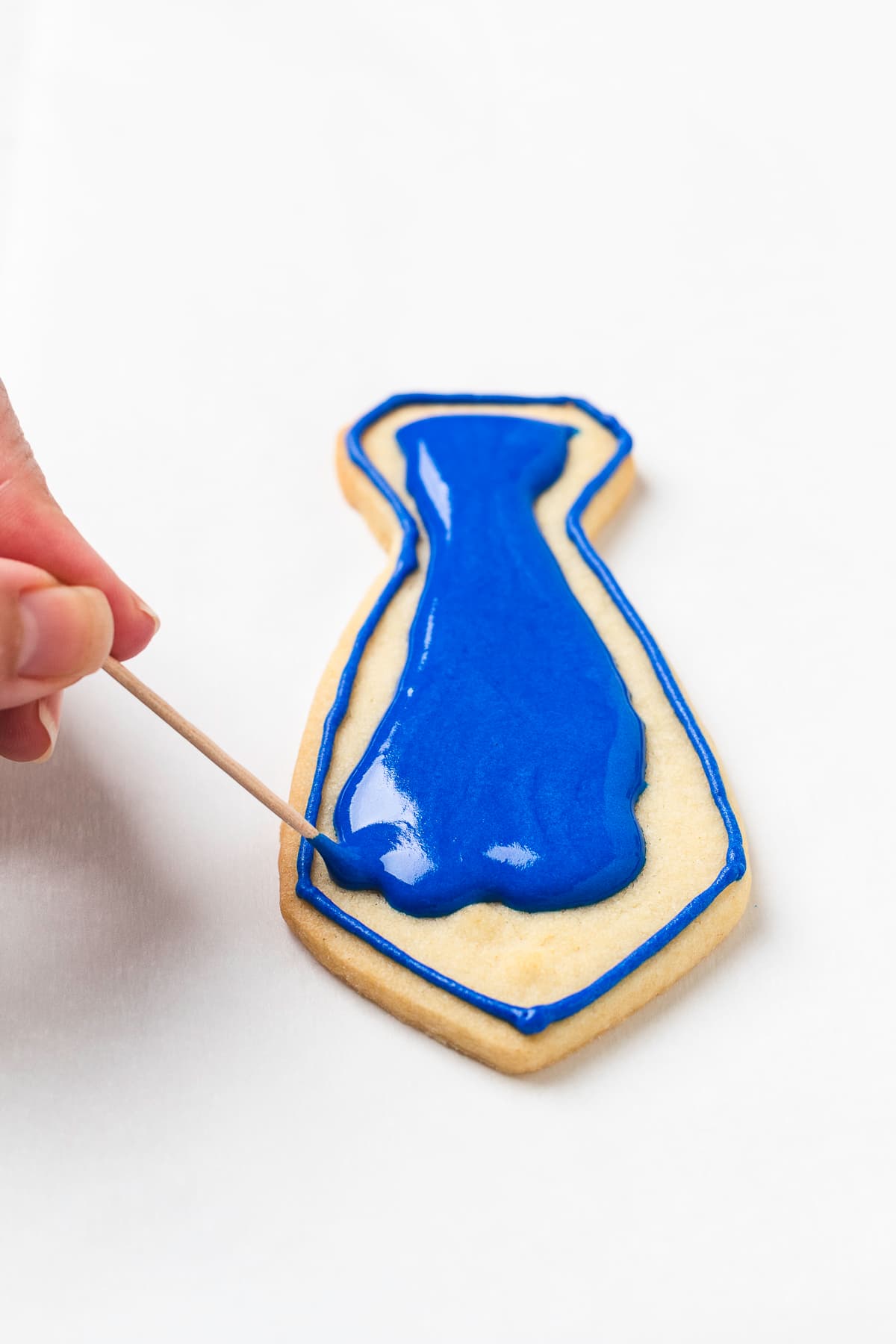 Hand spreading royal icing on necktie cookie.