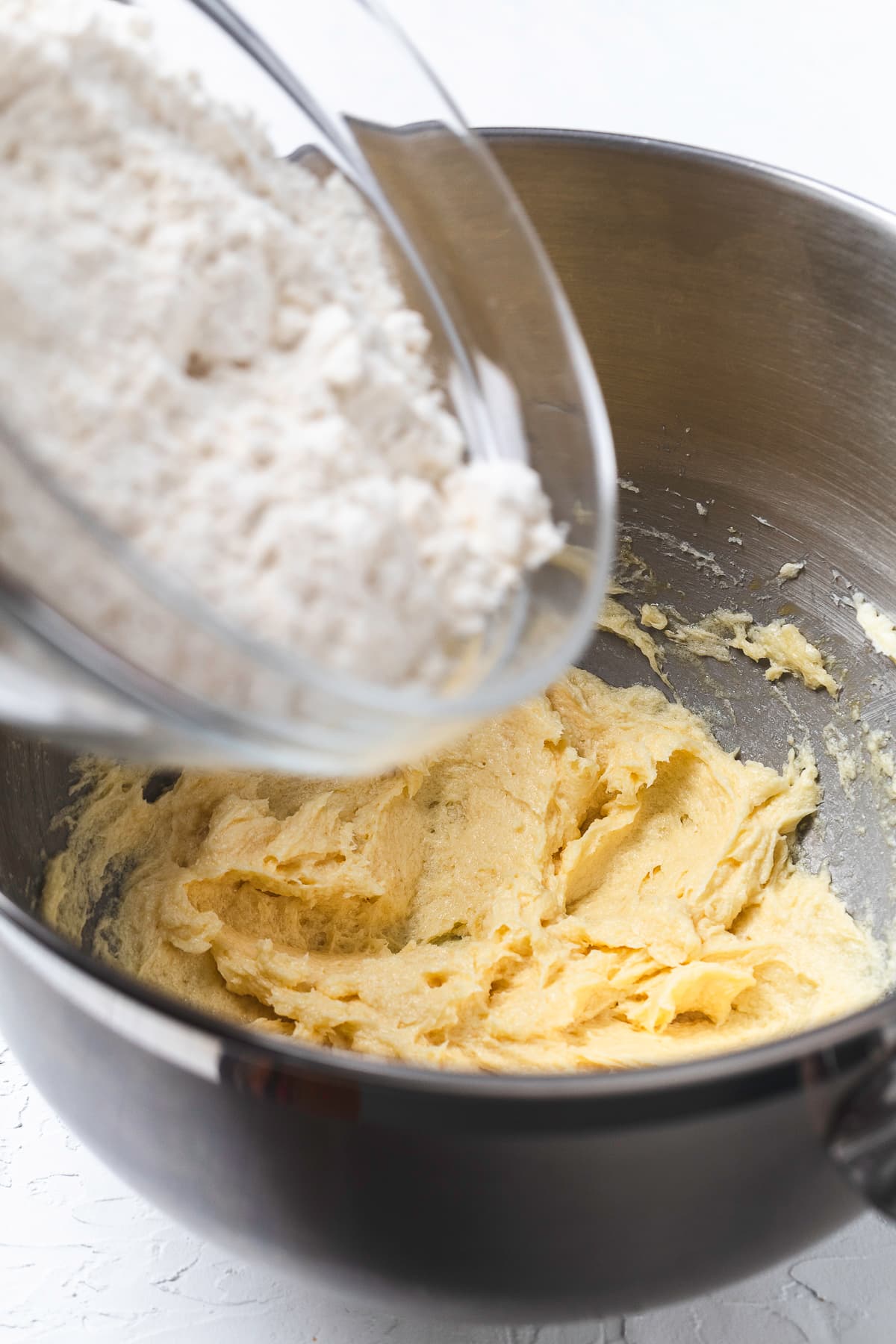 A raw egg and vanilla extract added to the creamed butter and sugar mixture in a bowl.