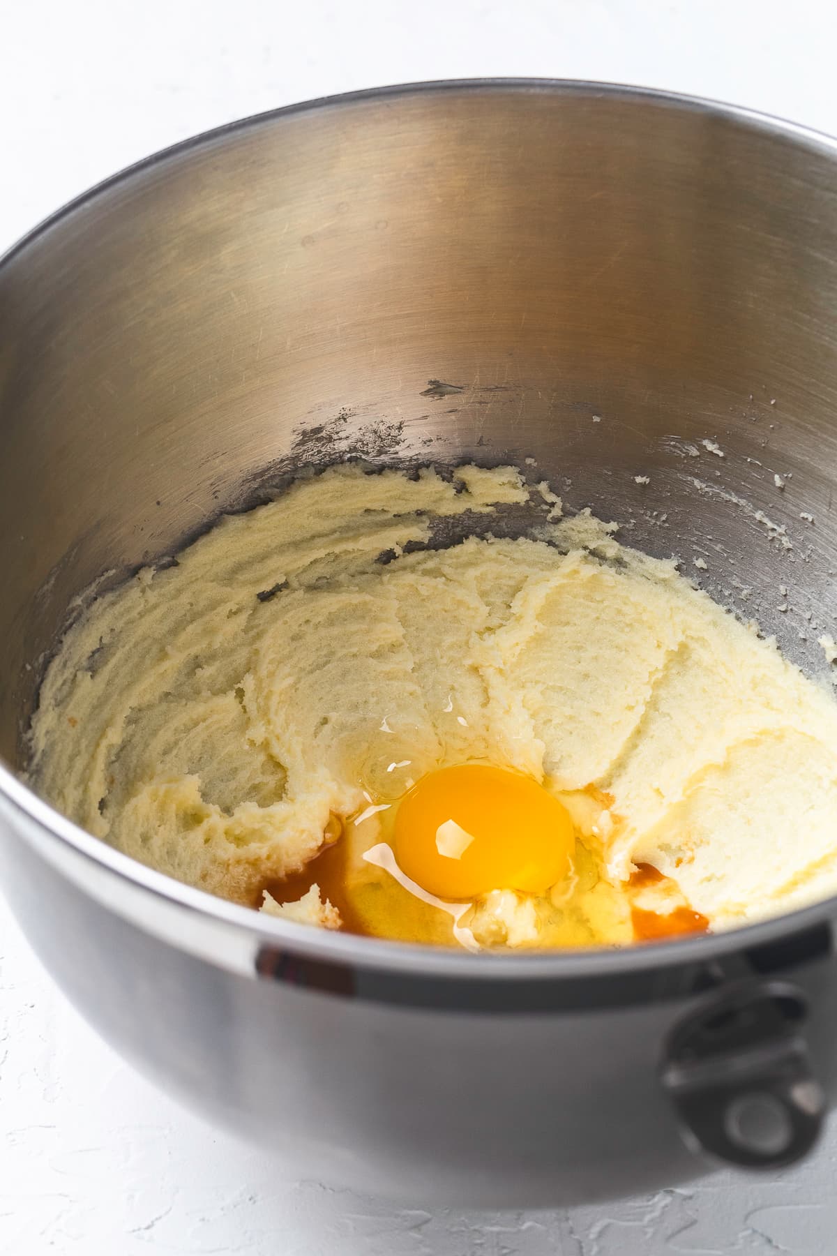 Flour being added to the creamed butter and sugar mixture in a metal mixing bowl.