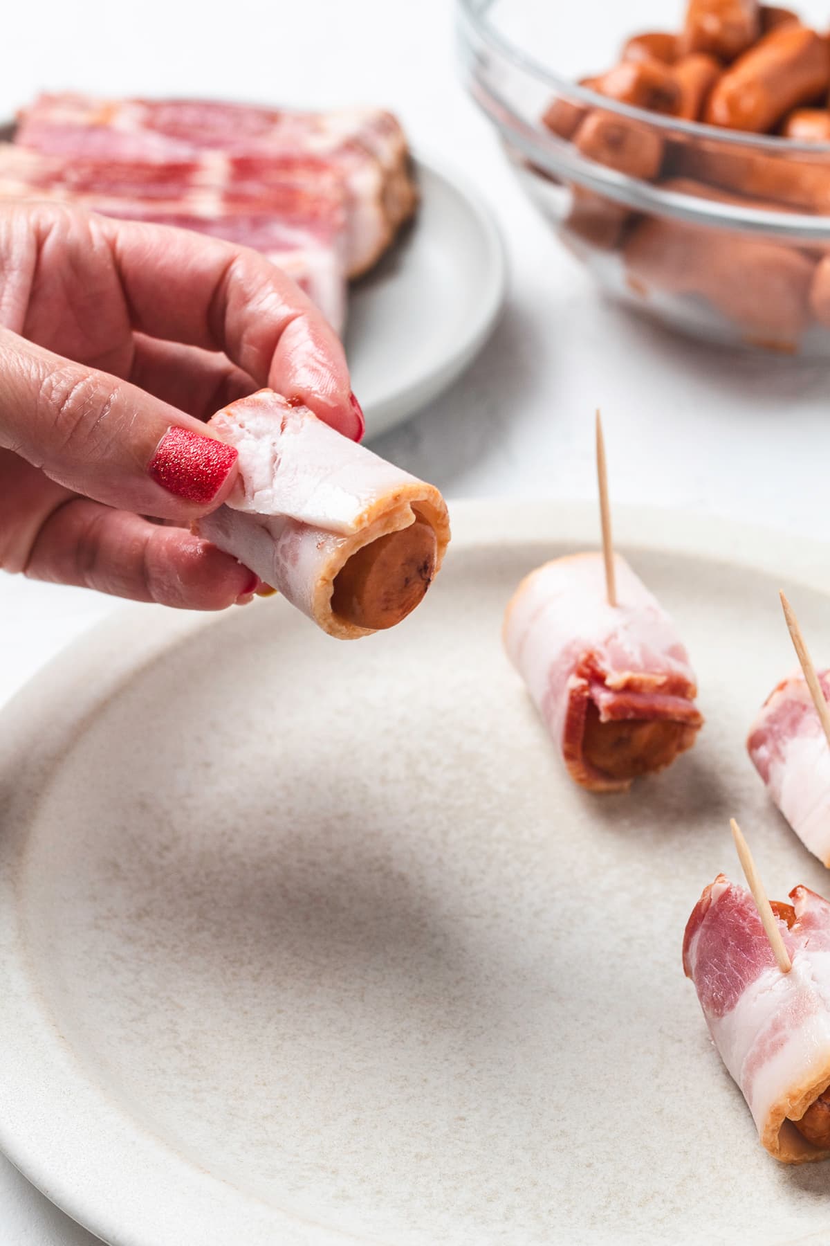 Hand holding bacon-wrapped sausage.
