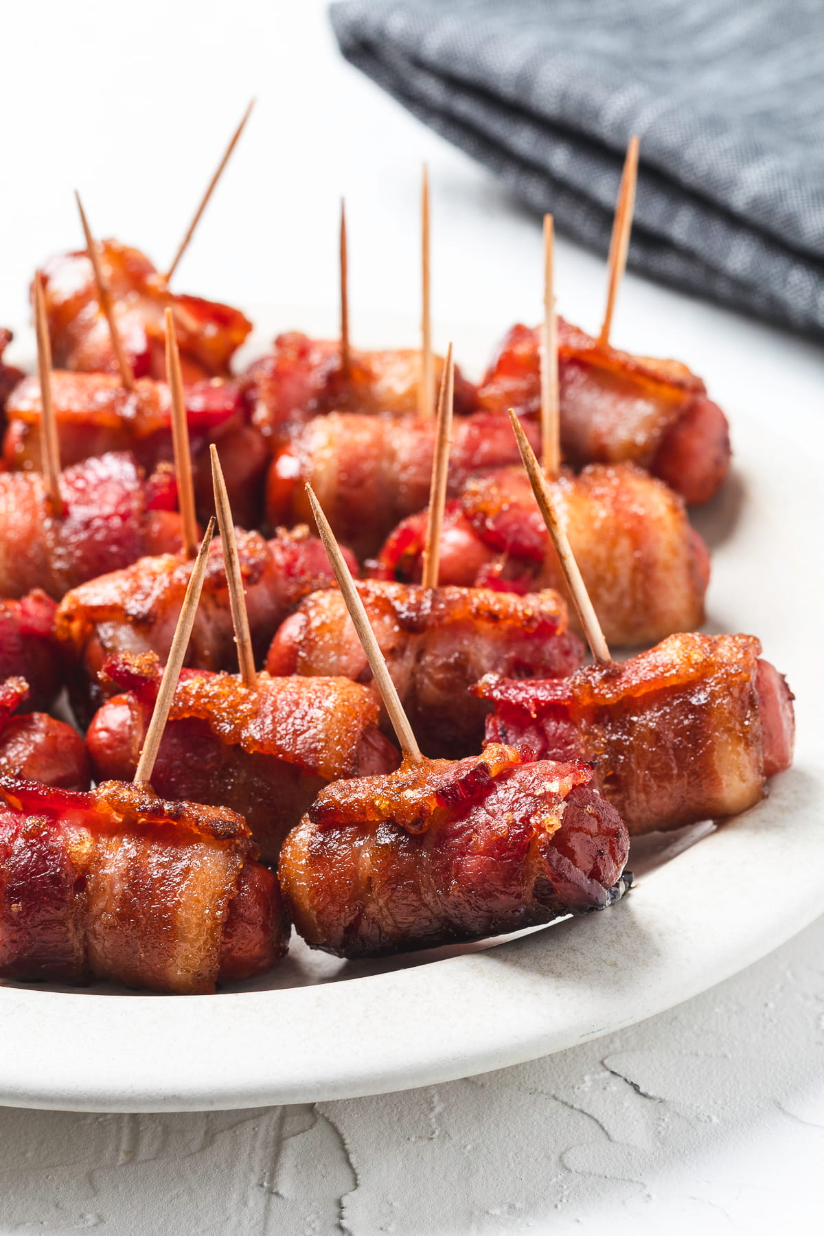 Cooked bacon-wrapped smokies with toothpicks on a plate.